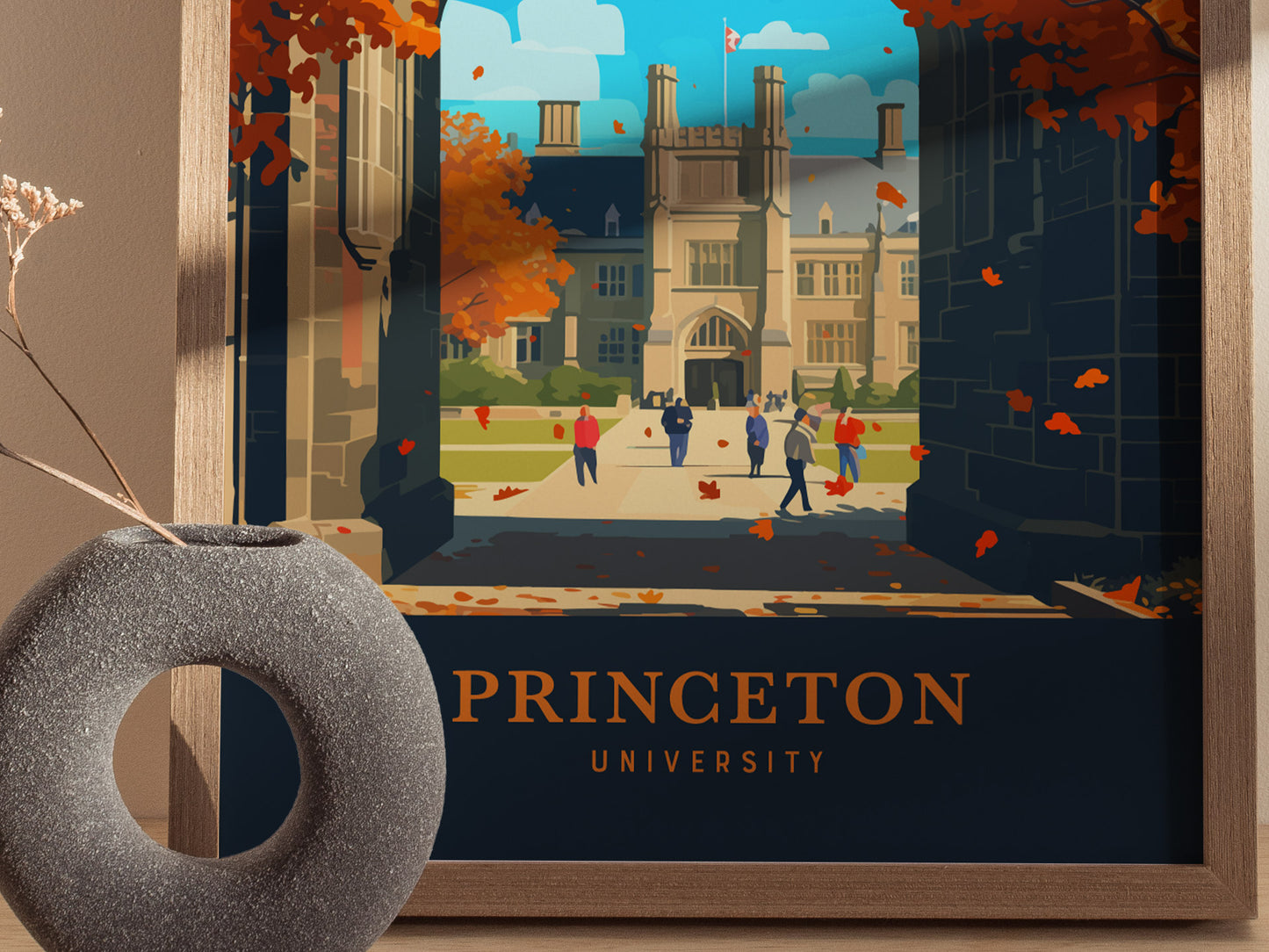 A framed poster featuring an illustration of Princeton University, showing a Gothic-style building, tree-lined walkways, and people walking. Autumn leaves are scattered, adding warmth to the scene.