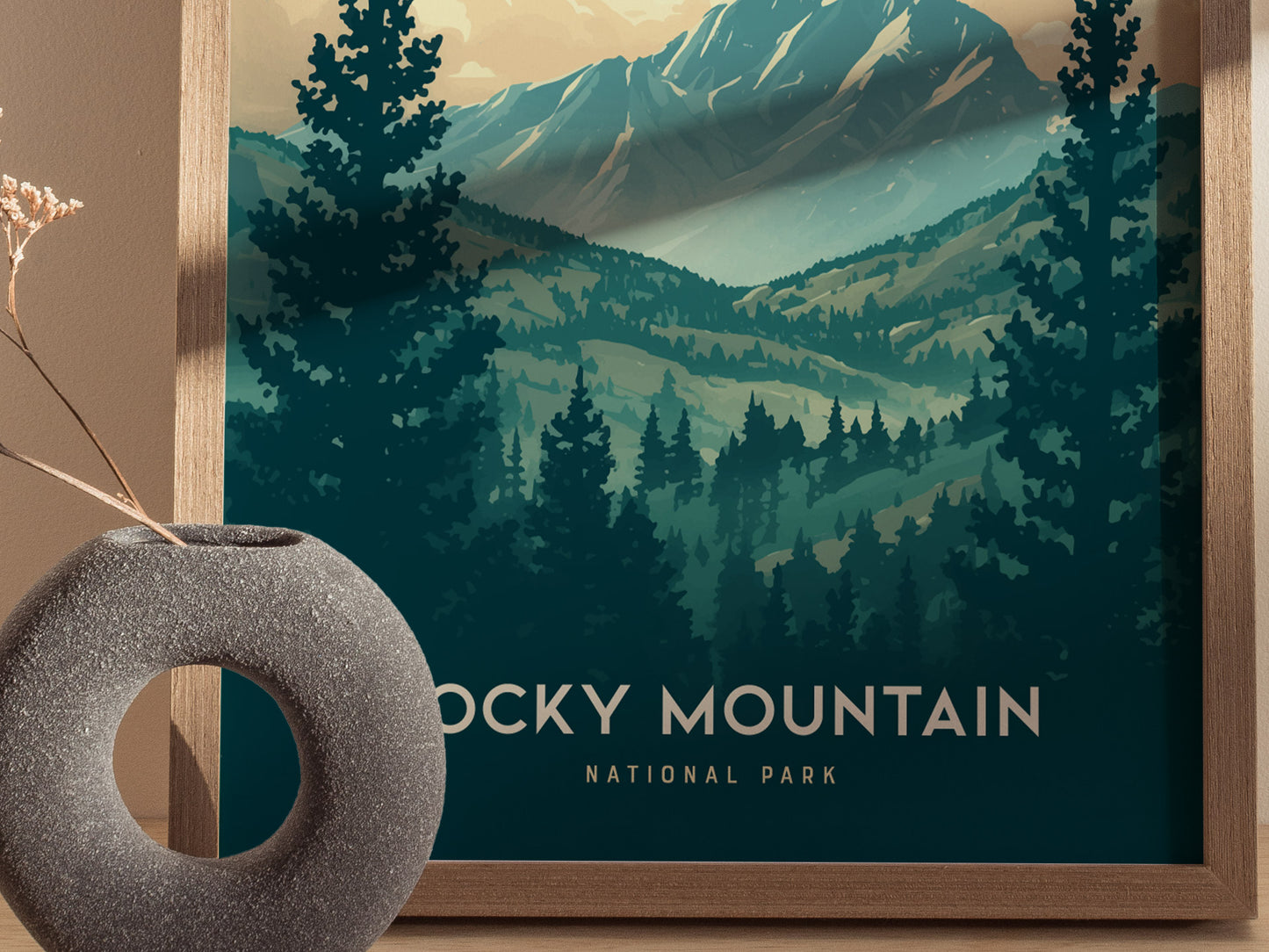 A framed poster of Rocky Mountain National Park features stylized mountains and lush forests. A round, textured vase with dried flowers is placed next to the poster.