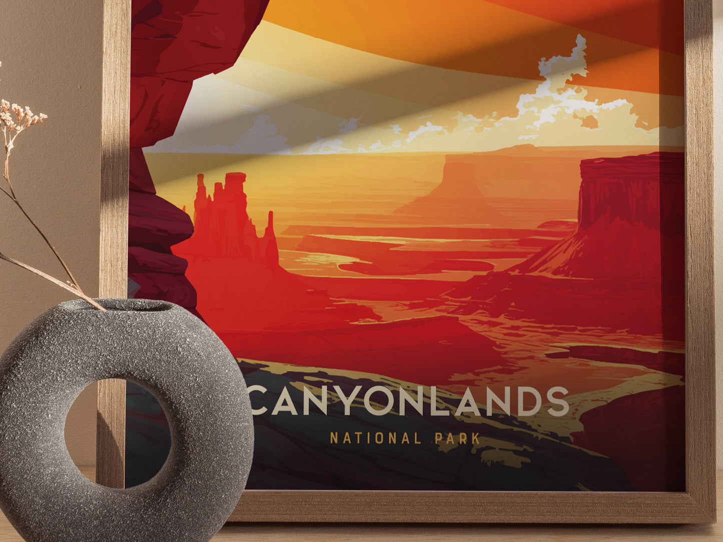 A framed Canyonlands National Park poster depicting vibrant red and orange desert canyons is displayed beside a textured, round vase with dried flowers.