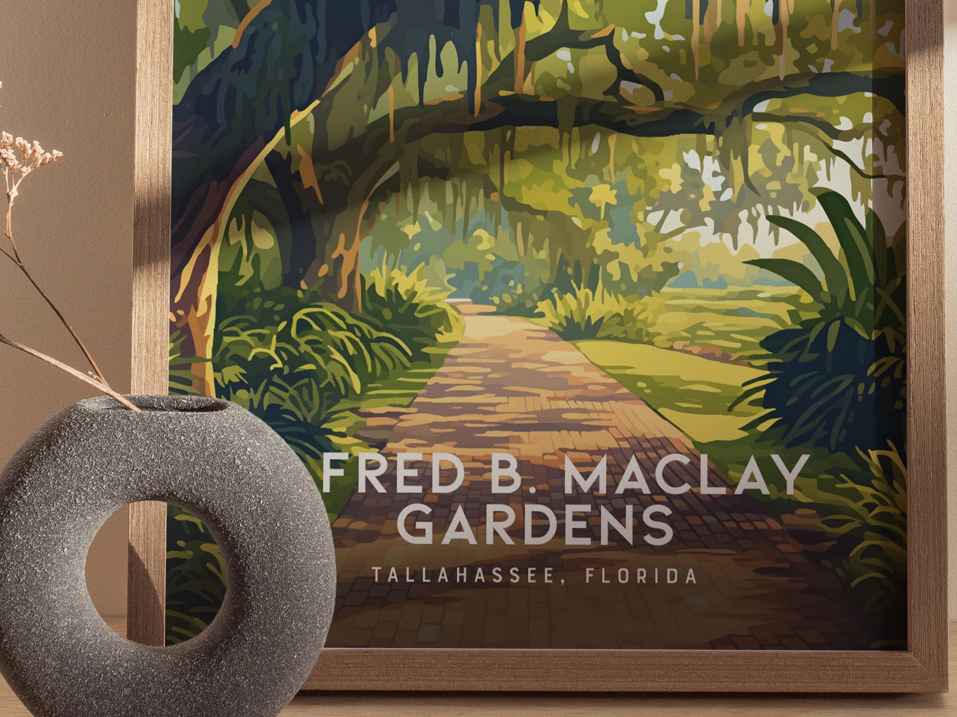 Framed illustration of Alfred B. Maclay Gardens features a winding brick path under moss-draped trees. A round, textured vase with dried flowers is placed in the foreground.