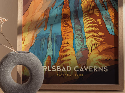A colorful Carlsbad Caverns National Park poster features vibrant rock formations, framed in wood. A textured gray vase with dried flowers sits nearby.