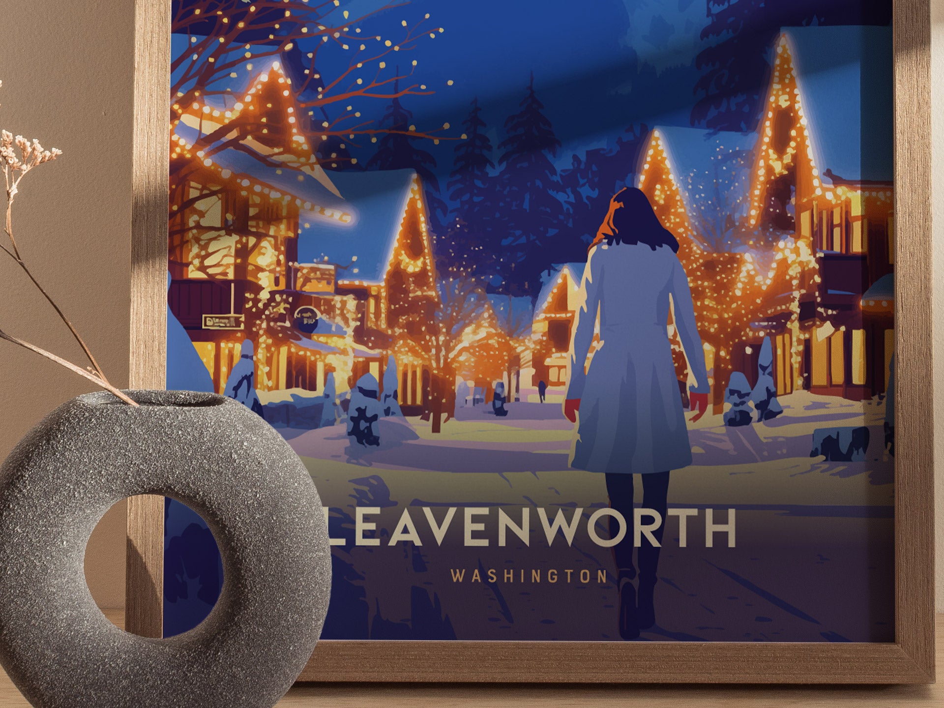 A framed poster depicts a person walking through a snowy village adorned with festive lights at night, with the words Leavenworth Washington visible below. A textured vase sits nearby.