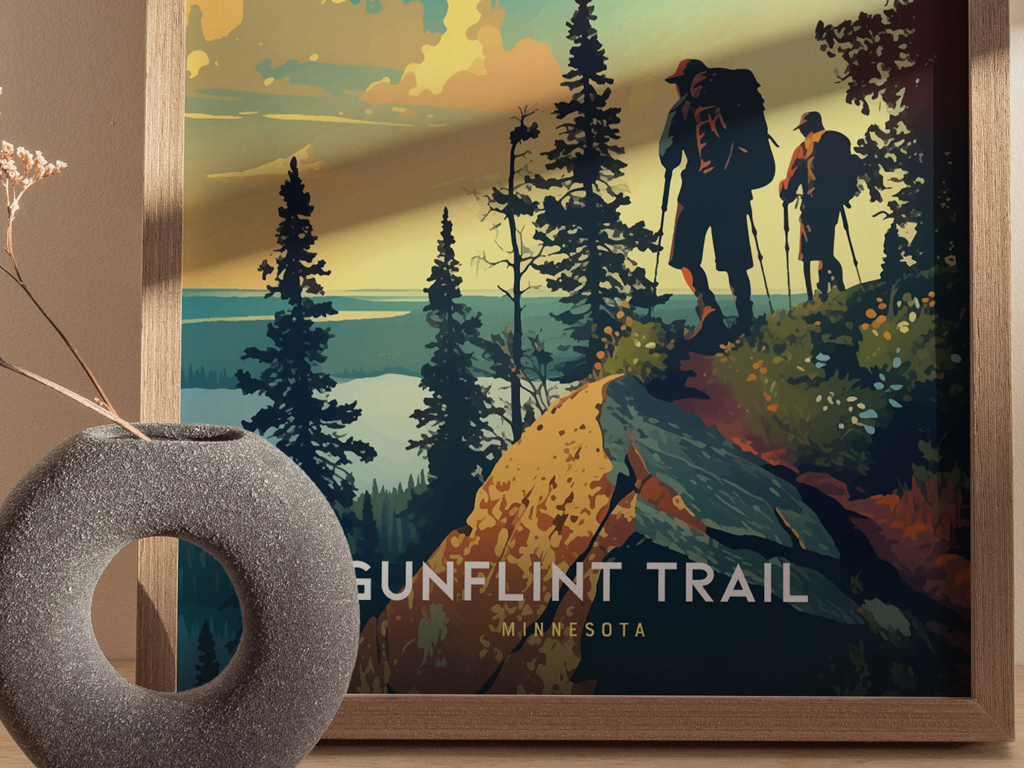 A poster titled Gunflint Trail Minnesota depicts two hikers on a scenic trail surrounded by trees and a colorful sky. A textured vase is in the foreground.