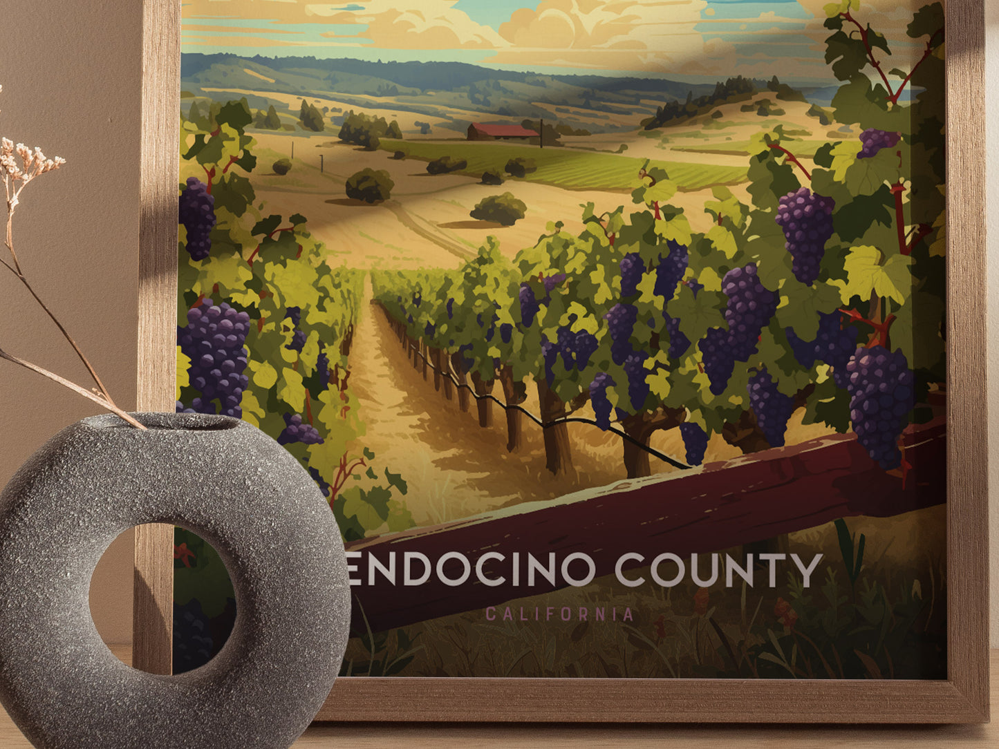 Framed poster of Mendocino County, featuring lush vineyards under a vibrant sky. A round, stone-textured vase with dried branches sits in the foreground, adding to the rustic charm.
