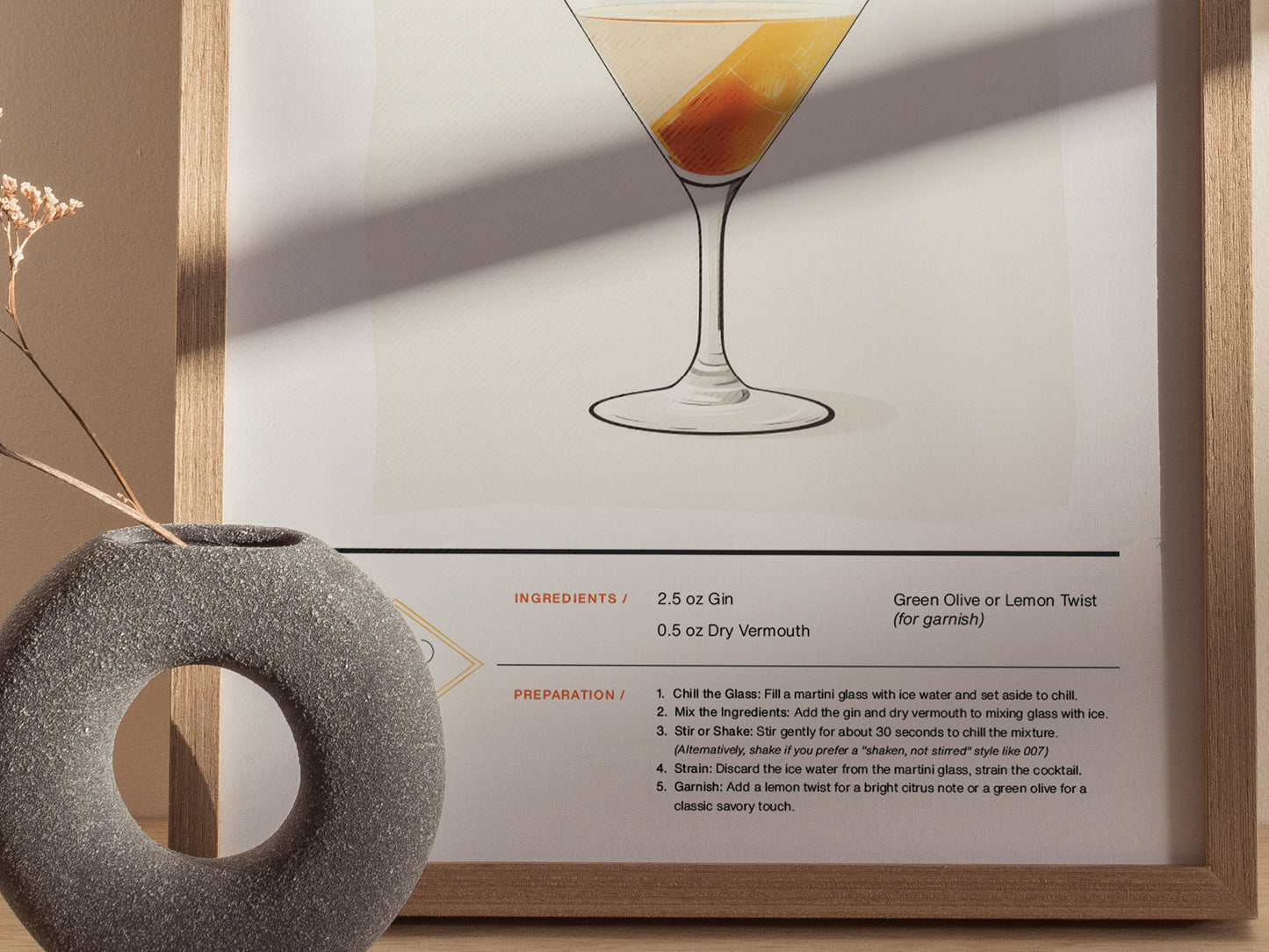 A framed martini cocktail poster features an illustrated martini glass above a classic dry martini recipe. A textured, round vase with dried flowers is nearby.
