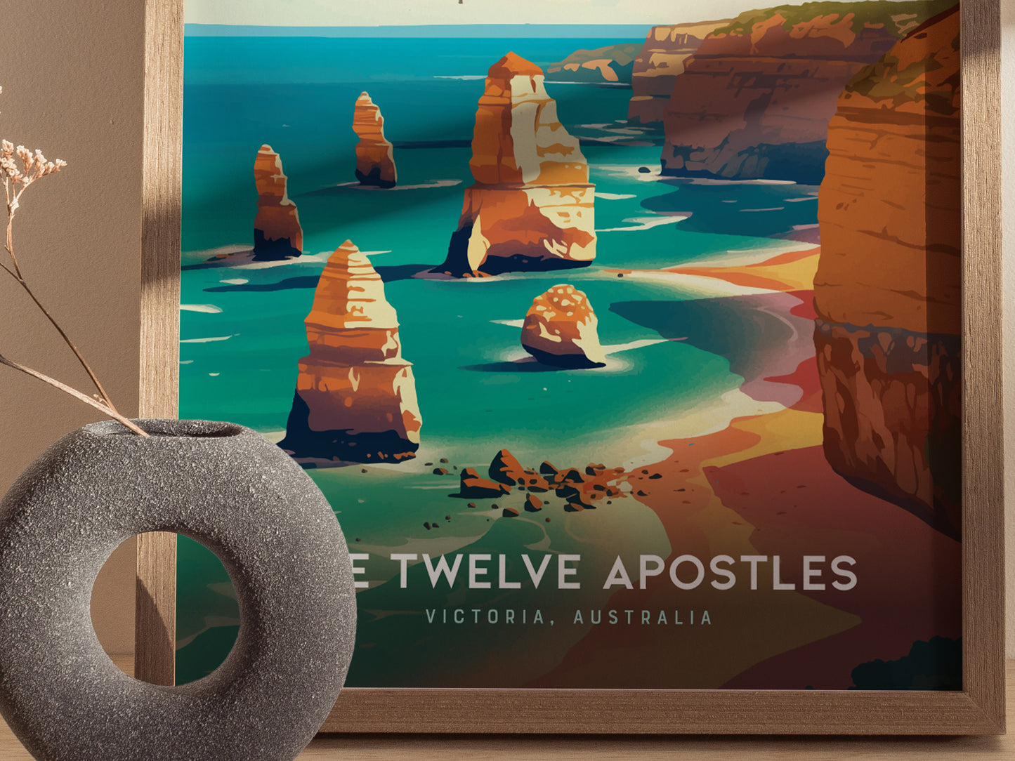 A framed poster depicts the Twelve Apostles, showcasing vibrant turquoise waters and towering limestone stacks along the coast. A modern, round vase with dried flowers sits nearby.