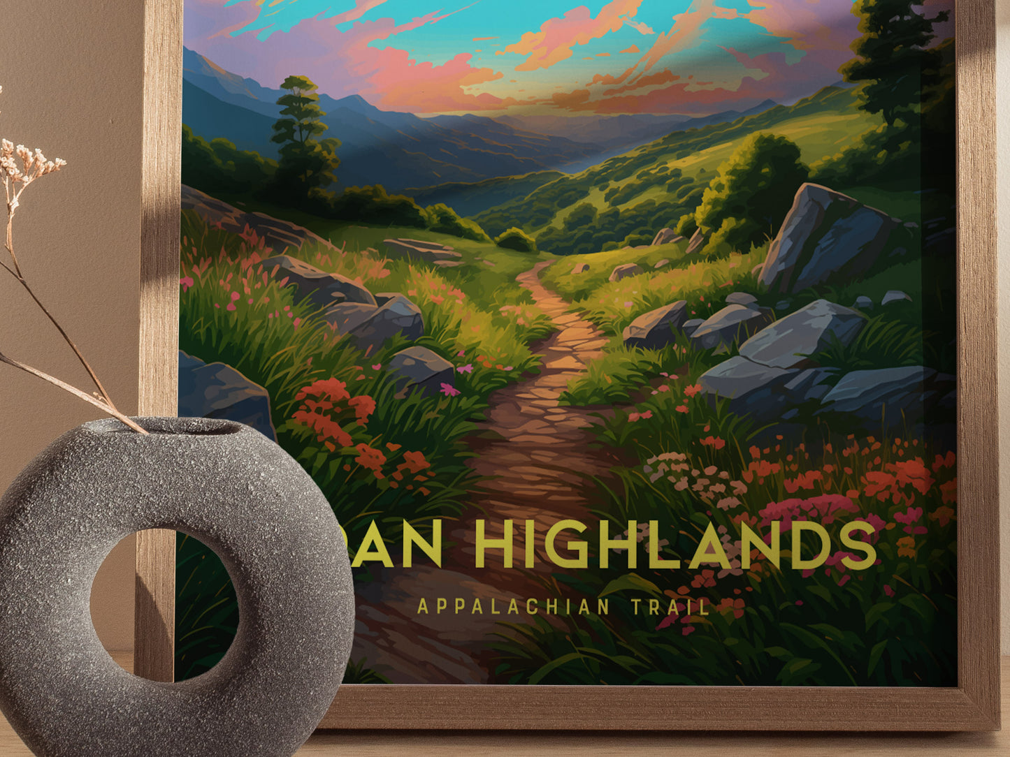 A framed poster depicting a colorful sunrise over a winding trail in the Roan Highlands, surrounded by lush greenery and wildflowers. A gray, circular vase is in the foreground.