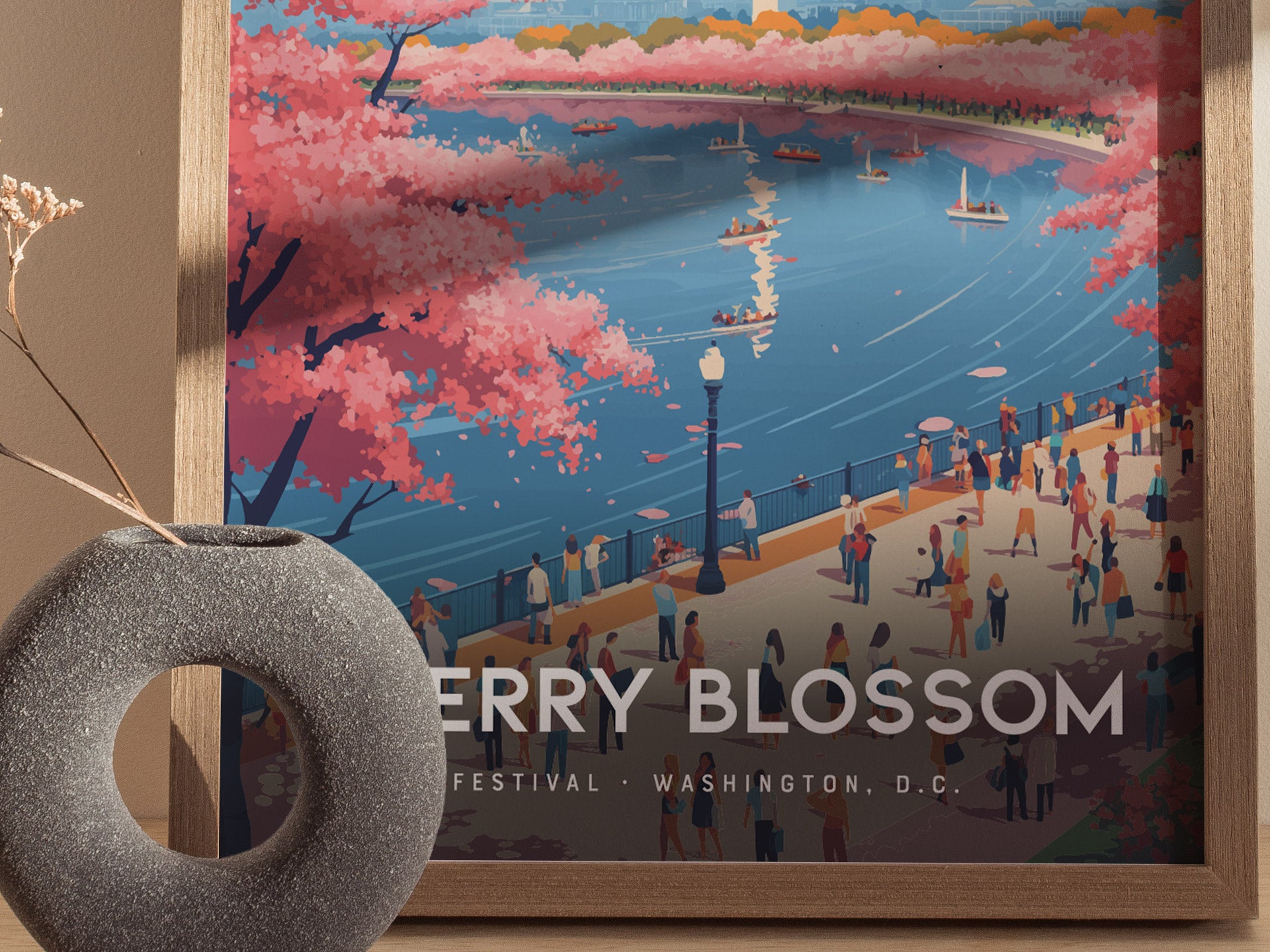 A framed poster depicts a vibrant scene of Washington D.C.s Cherry Blossom Festival, showcasing pink cherry trees along a river with boats and people enjoying the view.