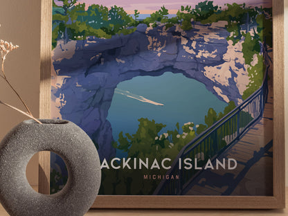 A framed poster of Mackinac Island Arch Rock, featuring a vibrant illustration of the limestone arch, lush greenery, and blue waters. A decorative vase is partially visible in the foreground.