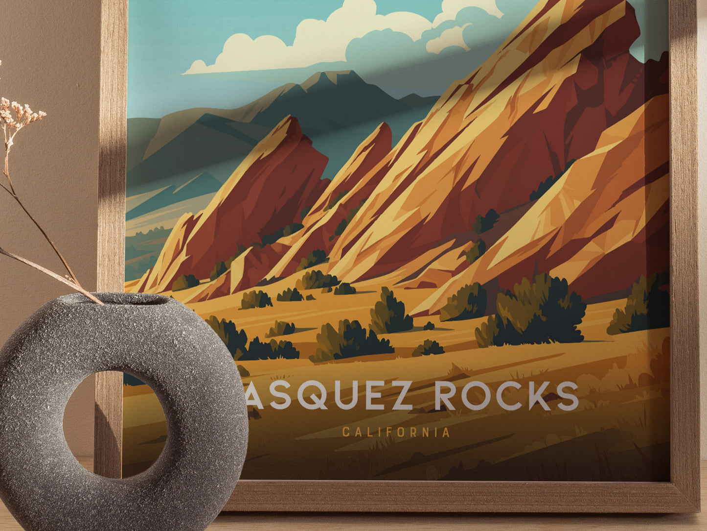 A framed Vasquez Rocks poster showcases vibrant, tilted sandstone formations under a blue sky. A textured, circular vase with dried flowers is placed in the foreground.