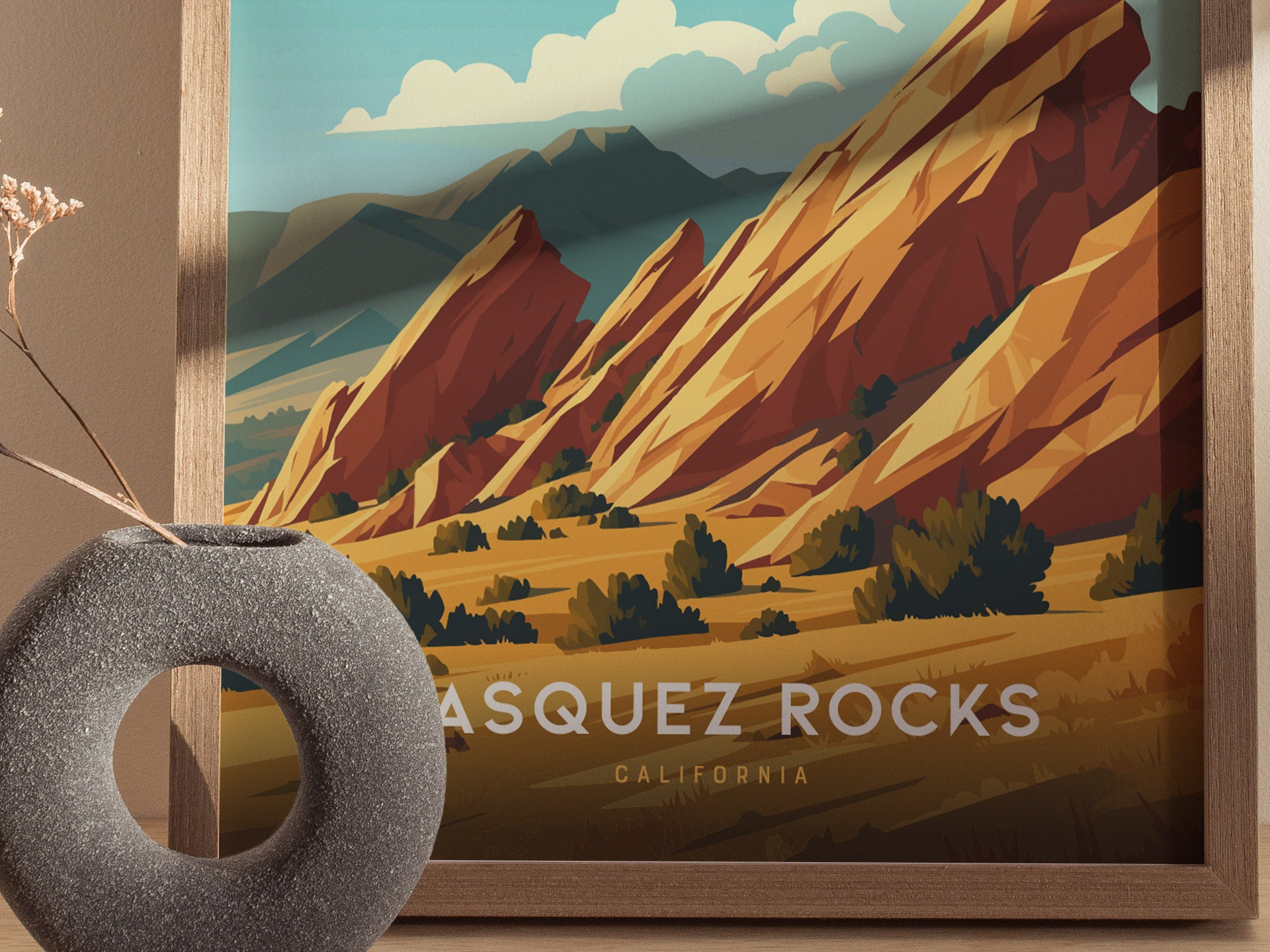 A framed Vasquez Rocks poster showcases vibrant, tilted sandstone formations under a blue sky. A textured, circular vase with dried flowers is placed in the foreground.