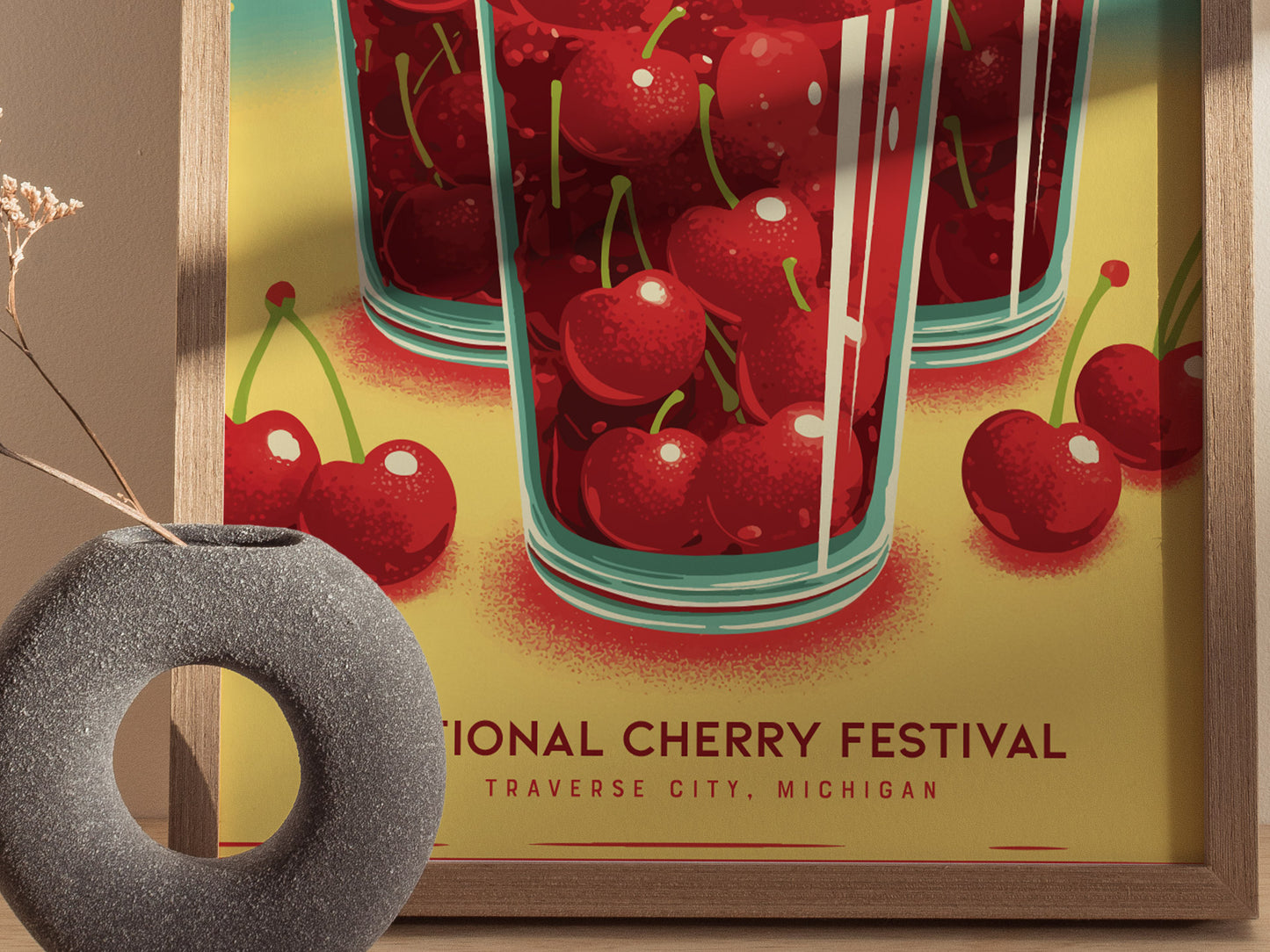 A vibrant poster for the National Cherry Festival in Traverse City, Michigan, features bright red cherries in glasses with a soft yellow background, framed in wood.