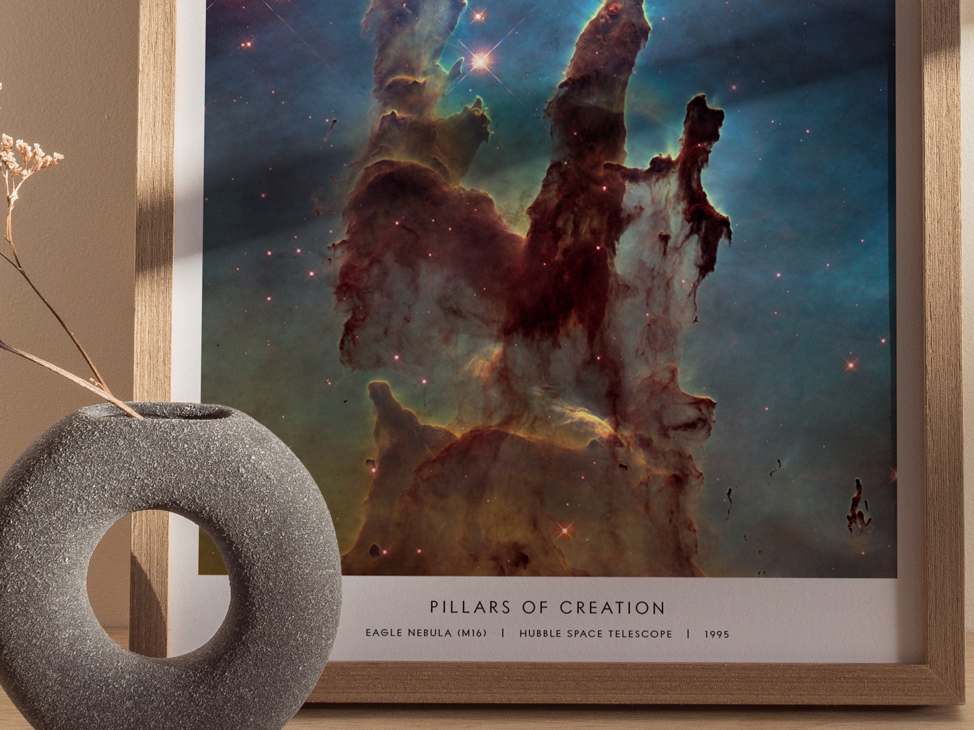 Framed space-themed artwork titled 'Pillars of Creation' with a decorative vase on a table.