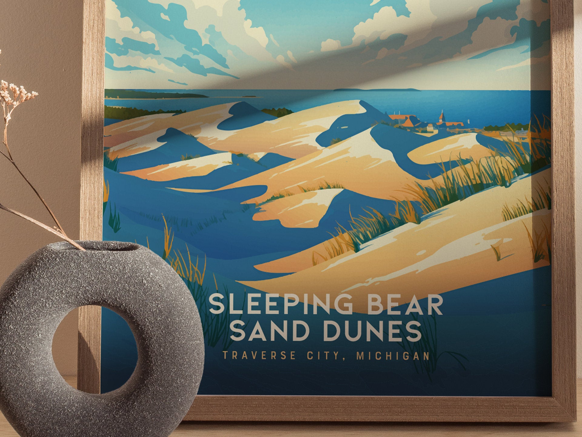 A framed poster of Sleeping Bear Sand Dunes depicts rolling sand dunes under a partly cloudy sky, with vibrant blue and golden tones.