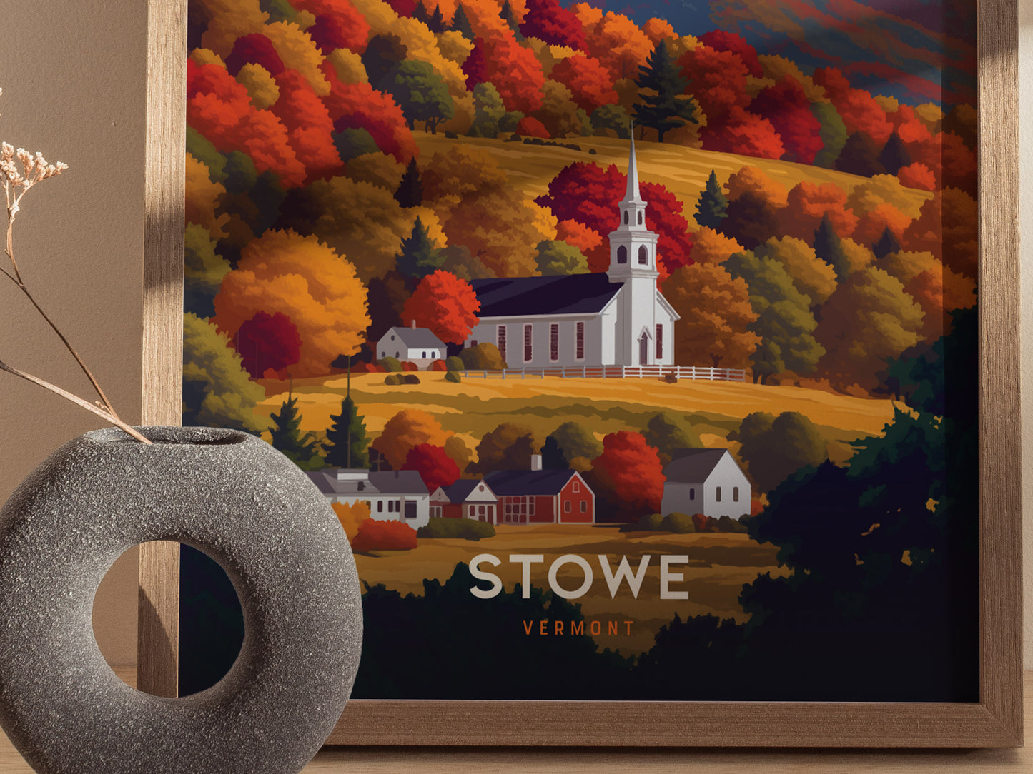 A framed poster depicts a white church steeple surrounded by vibrant fall foliage in shades of orange, red, and gold in Stowe, Vermont. A modern vase sits in the foreground.