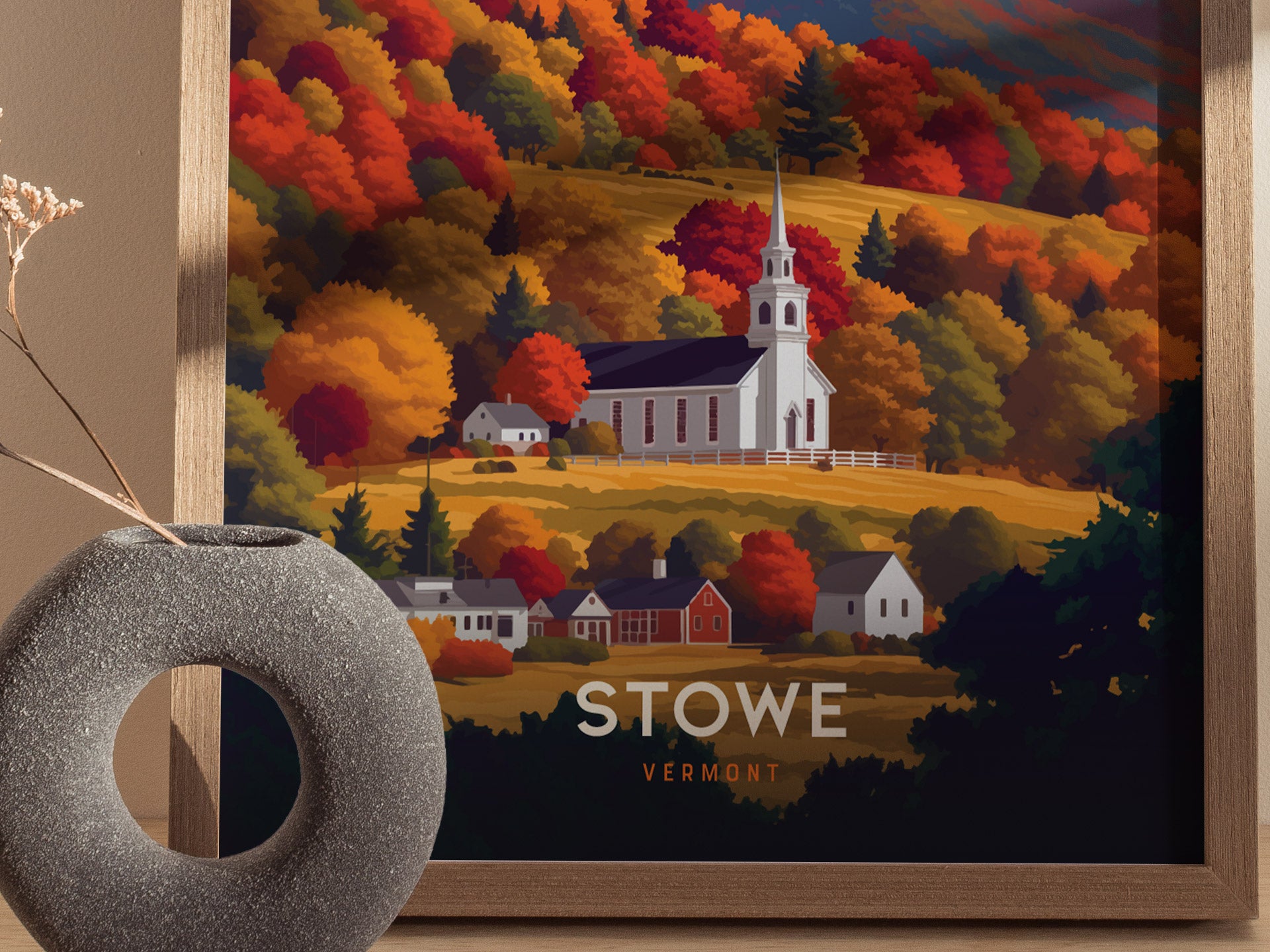 A framed poster depicts a white church steeple surrounded by vibrant fall foliage in shades of orange, red, and gold in Stowe, Vermont. A modern vase sits in the foreground.