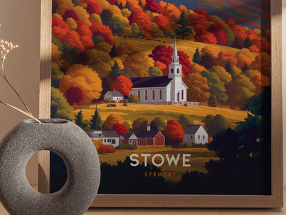 A framed poster depicts a white church steeple surrounded by vibrant fall foliage in shades of orange, red, and gold in Stowe, Vermont. A modern vase sits in the foreground.