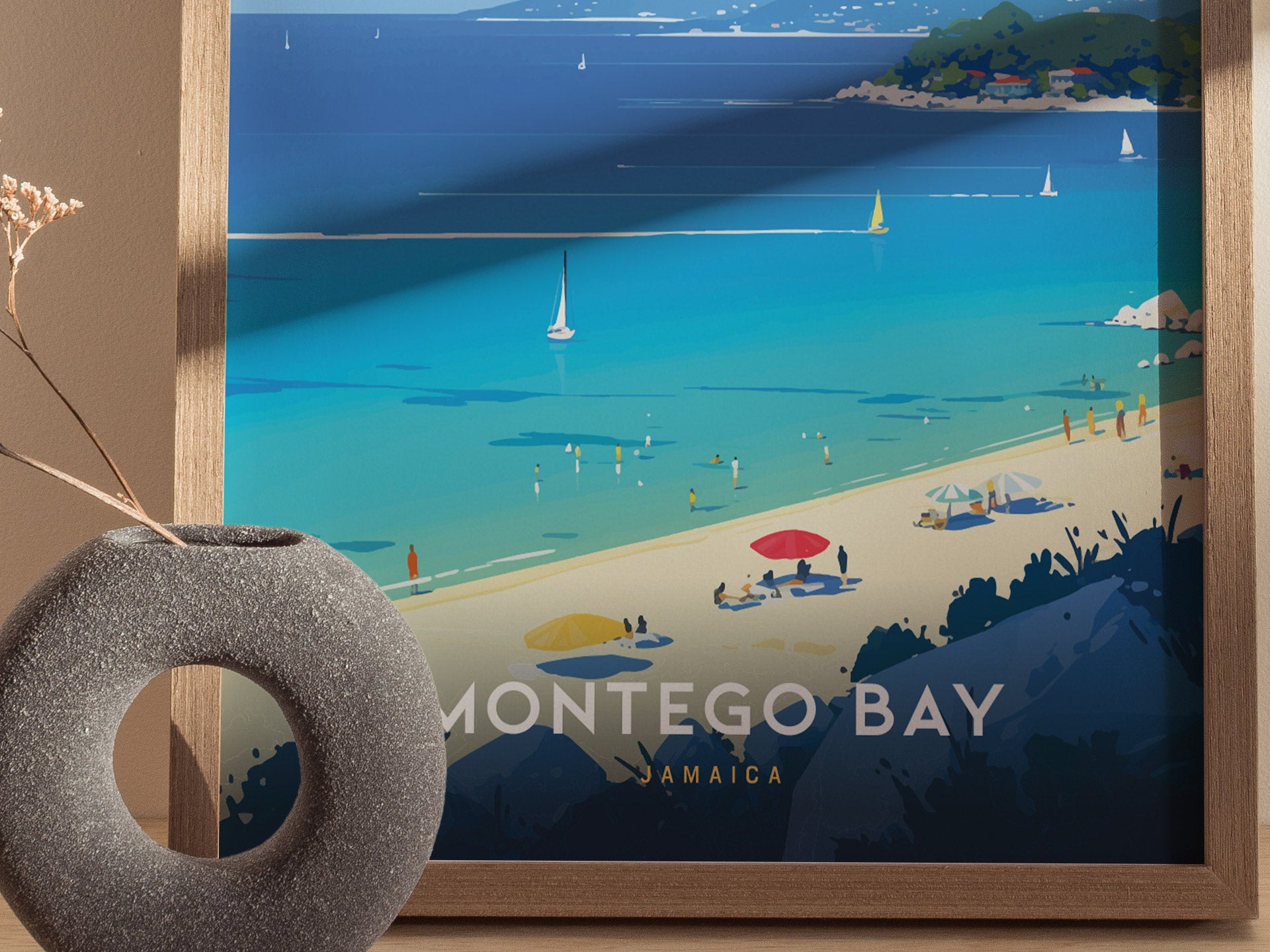 A framed poster of Montego Bay, Jamaica, displays a vibrant beach scene with turquoise waters, sailboats, and sunbathers. A textured vase sits in the foreground.