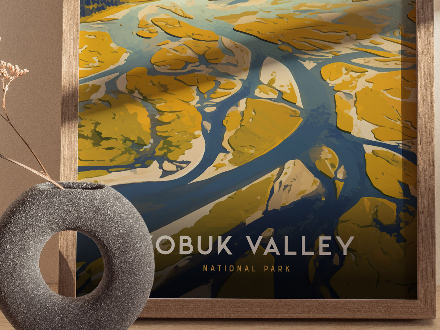 A framed poster of Kobuk Valley National Park features stylized blue rivers and yellow sand dunes, with a textured gray vase in the foreground.
