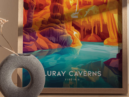 A framed poster of Luray Caverns features vibrant orange and purple cave formations above a reflective turquoise pool. A circular stone vase with dried flowers is nearby.