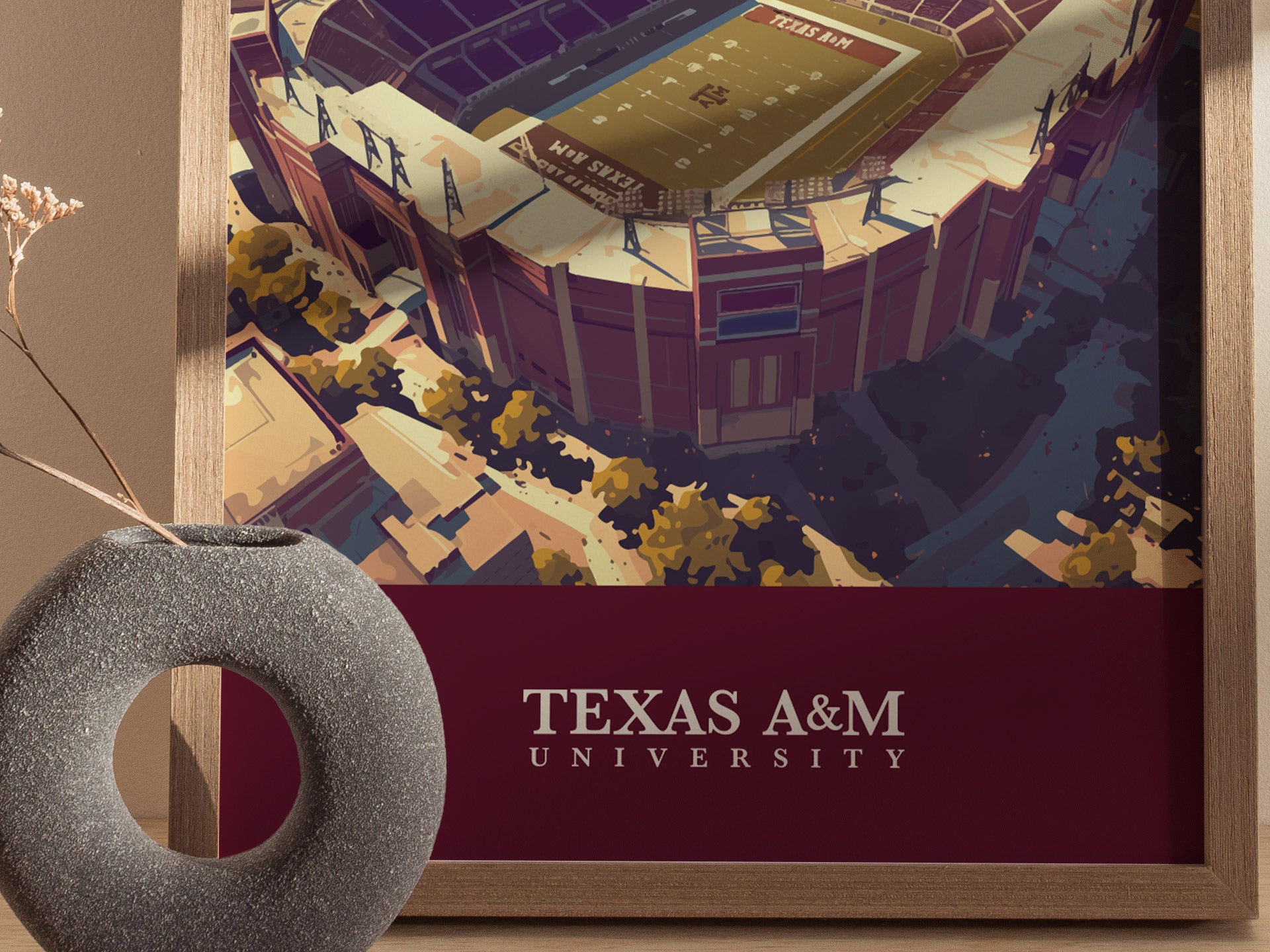 A framed poster of Kyle Field, Texas A&M Universitys stadium, is displayed alongside a decorative stone vase. The artwork highlights the stadiums architectural details and surrounding landscape.