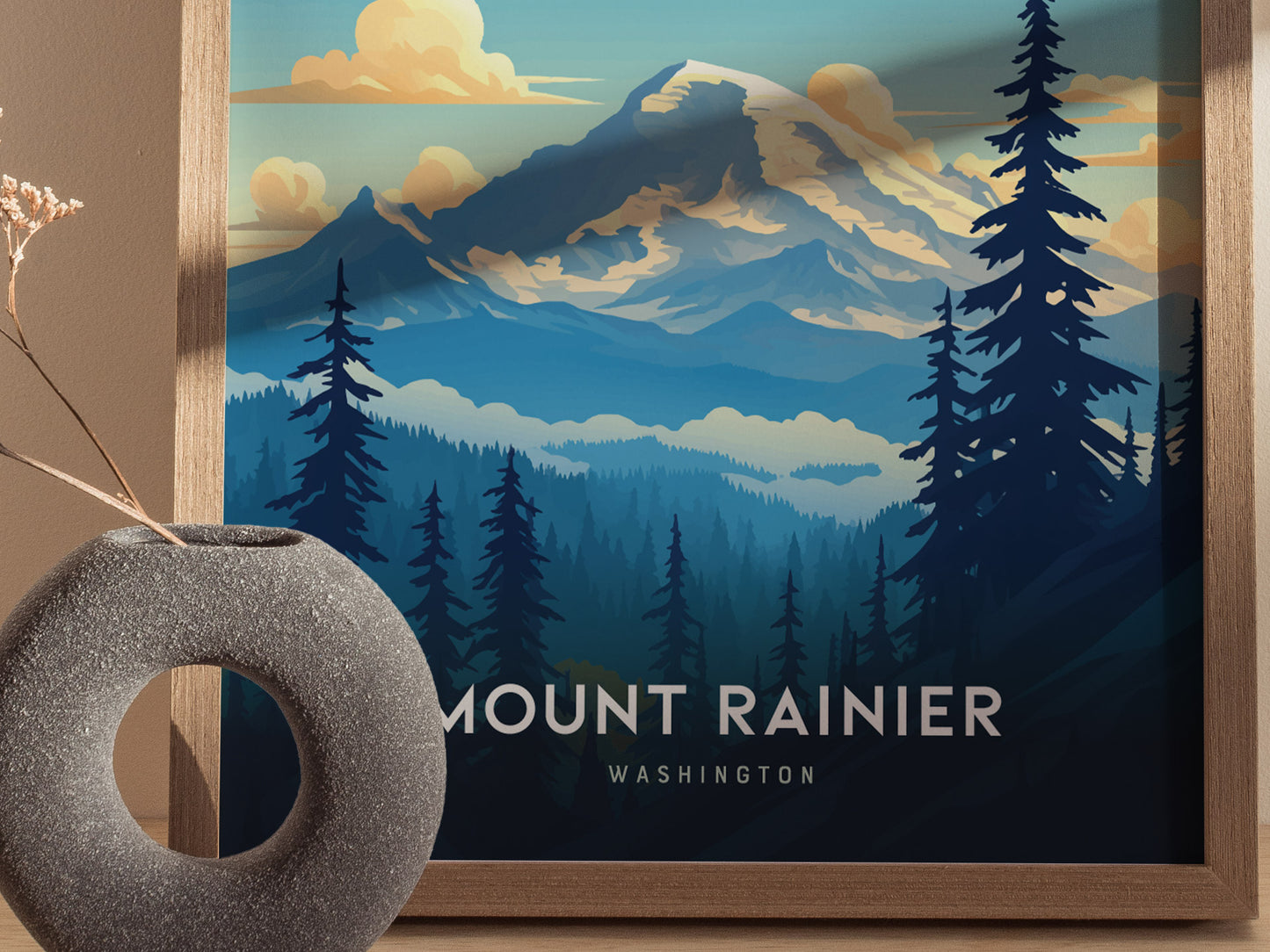 A framed poster features a stylized illustration of Mount Rainier with silhouetted trees and a cloudy sky. A textured gray vase with dried flowers is in the foreground.