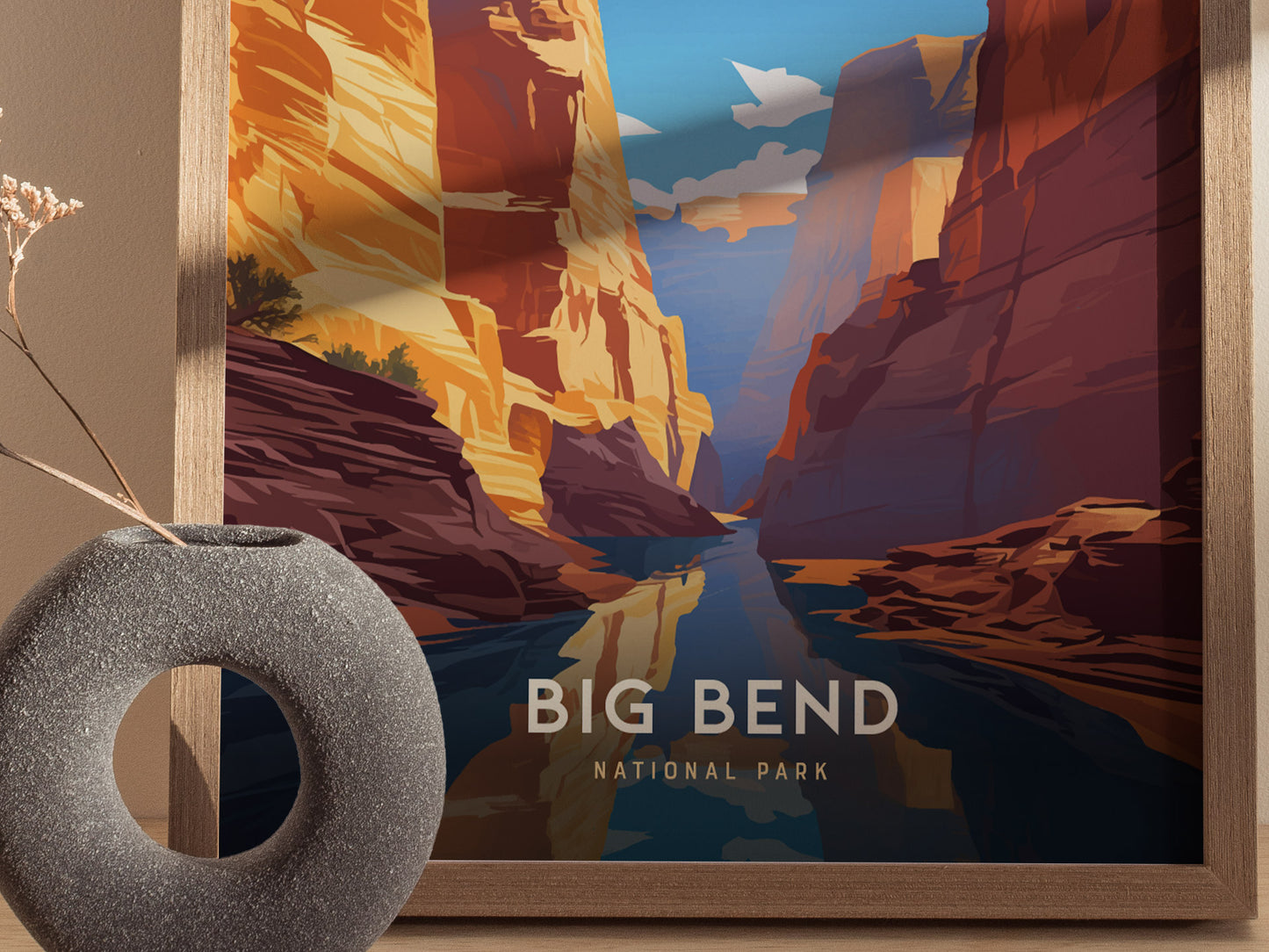 A framed poster of Big Bend National Park showcases colorful, dramatic canyons and a reflective river. A textured, round vase with dried flowers is positioned in front.