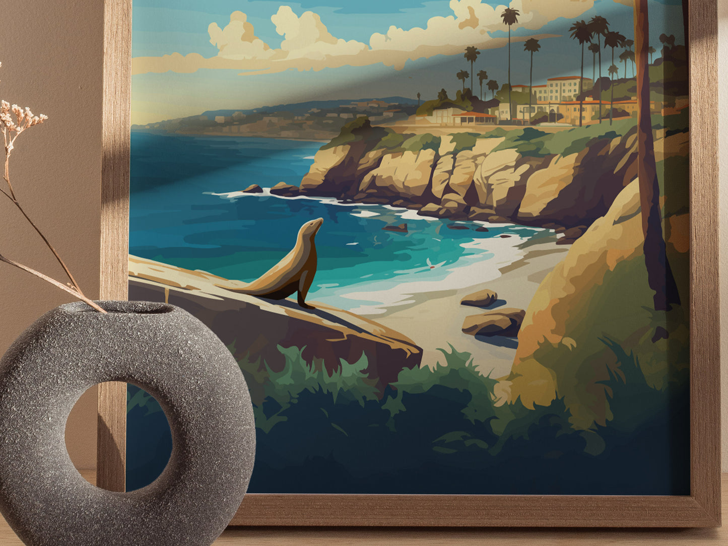 A framed poster depicting a scenic view of La Jolla Cove with sea cliffs, ocean waves, and a lone sea lion basking on a rock, alongside a textured circular vase.