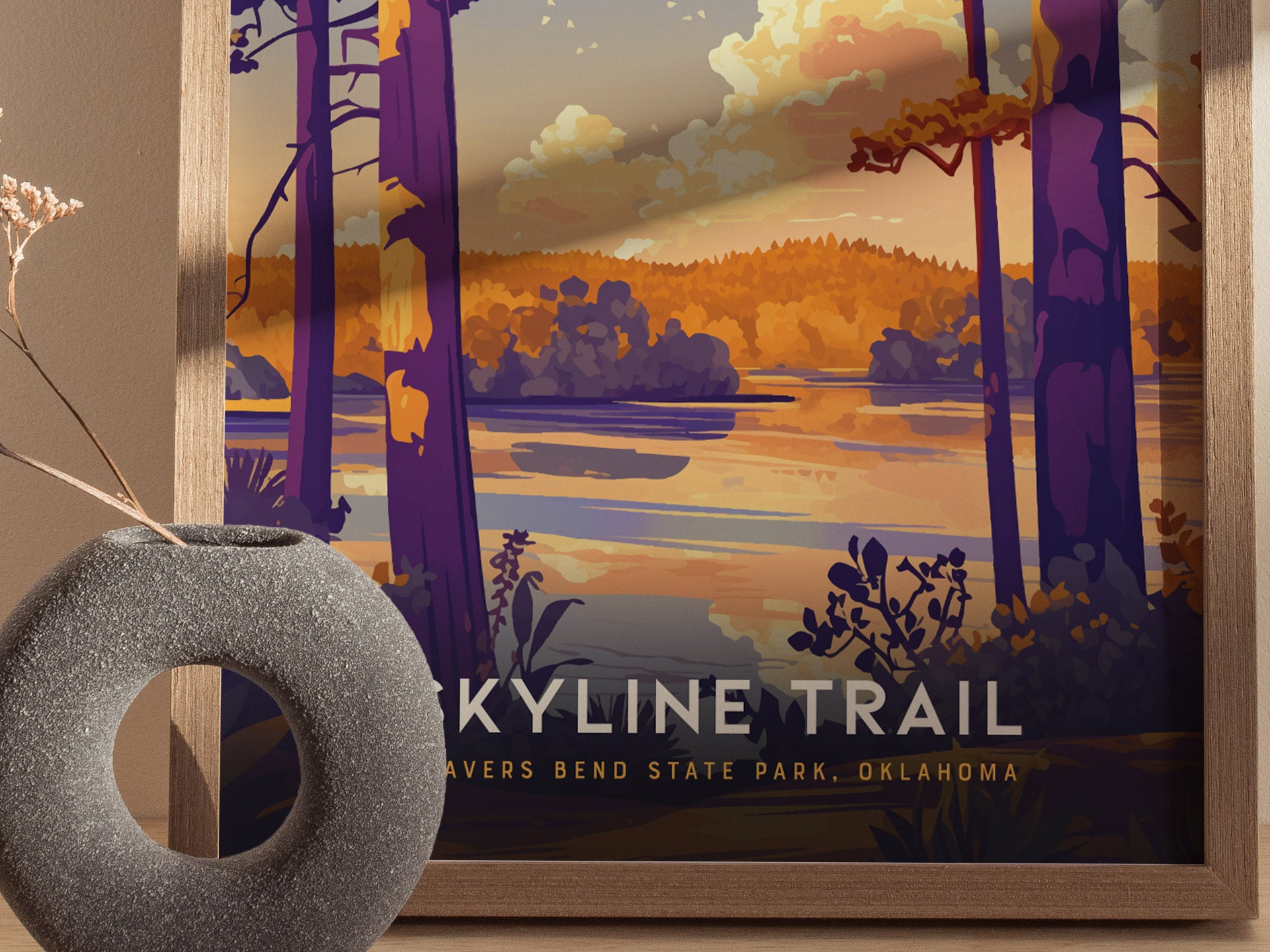 A framed poster depicts a scenic view of Beavers Bend State Park with vibrant trees and a tranquil lake at sunset. A textured, circular vase is positioned in the foreground.