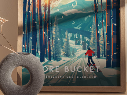 A framed poster depicts a skier in a red jacket navigating a snowy, tree-lined trail toward distant mountains. A textured vase with dried flowers sits beside the poster.
