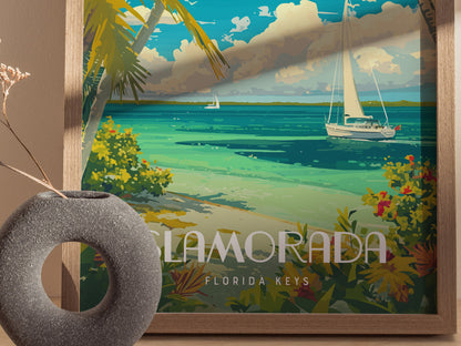 A framed poster of Islamorada, Florida Keys, features a sailboat on turquoise waters, tropical plants, and palm trees. A textured gray vase with dried flowers is in the foreground.