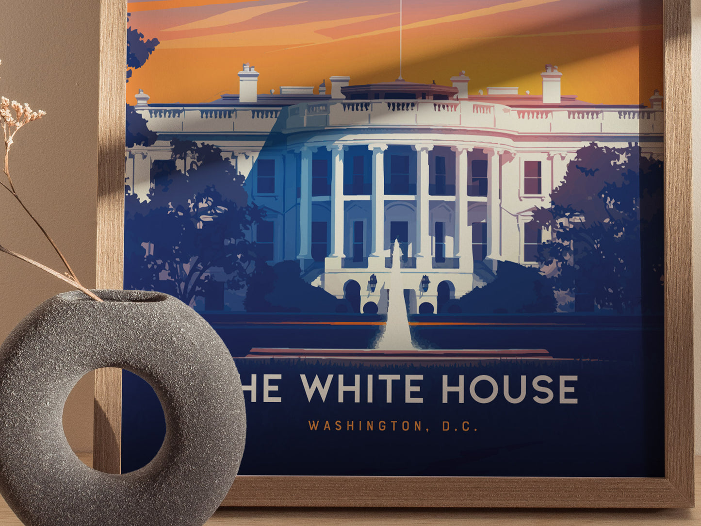 A framed poster of the White House with vibrant colors and minimalist design is displayed next to a textured, circular vase with dried flowers.