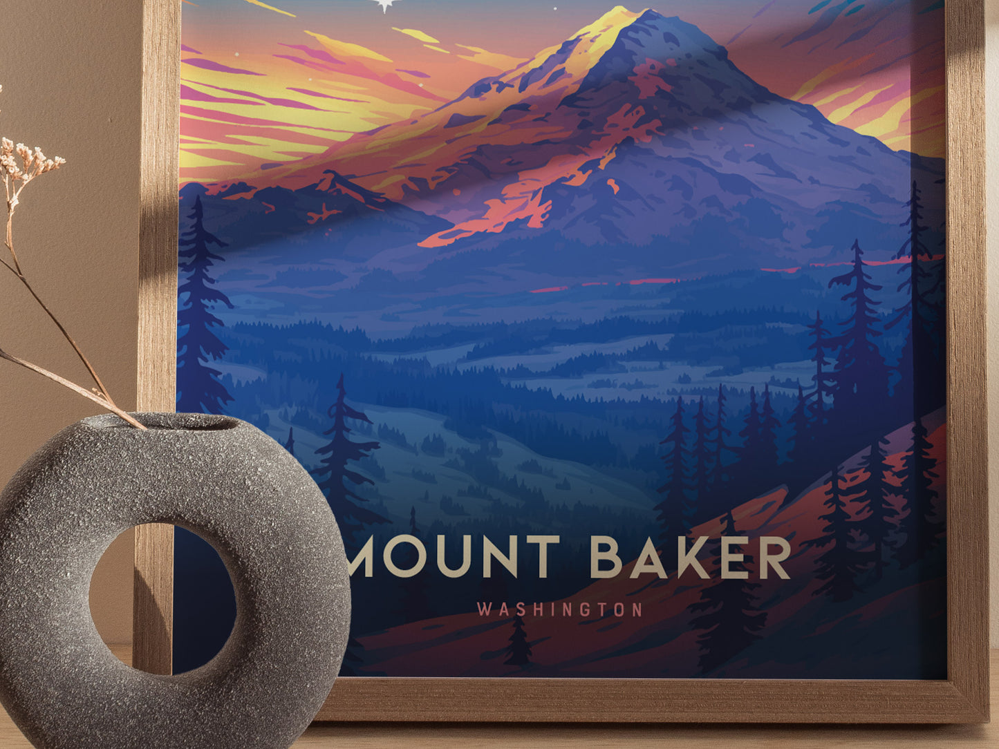 The image shows a framed Mount Baker poster with vibrant colors depicting the mountain at sunset. A textured, circular vase with dried flowers is positioned in the foreground.
