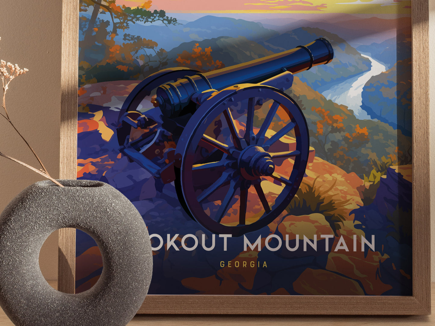 A framed poster features a cannon overlooking a scenic mountain landscape at sunset, with the words Lookout Mountain Georgia visible. A textured circular vase is in the foreground.