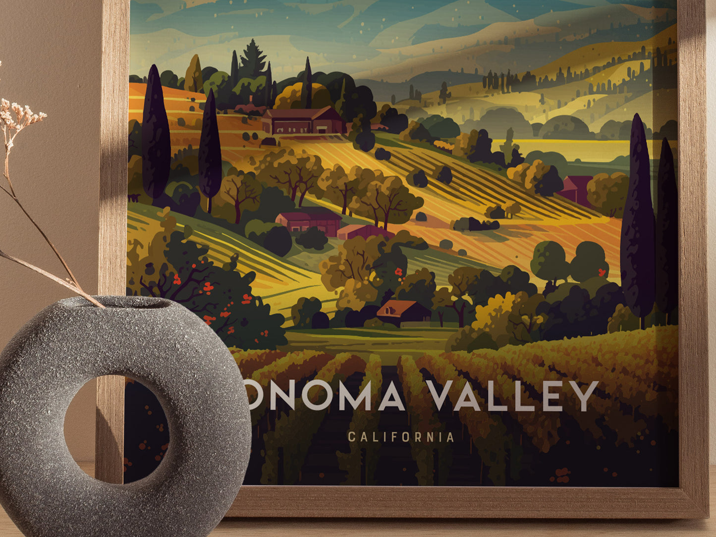 A framed poster depicts the Sonoma Valley with rolling vineyard hills in warm earth tones and lush greenery. A circular gray vase with dried flowers is in the foreground.