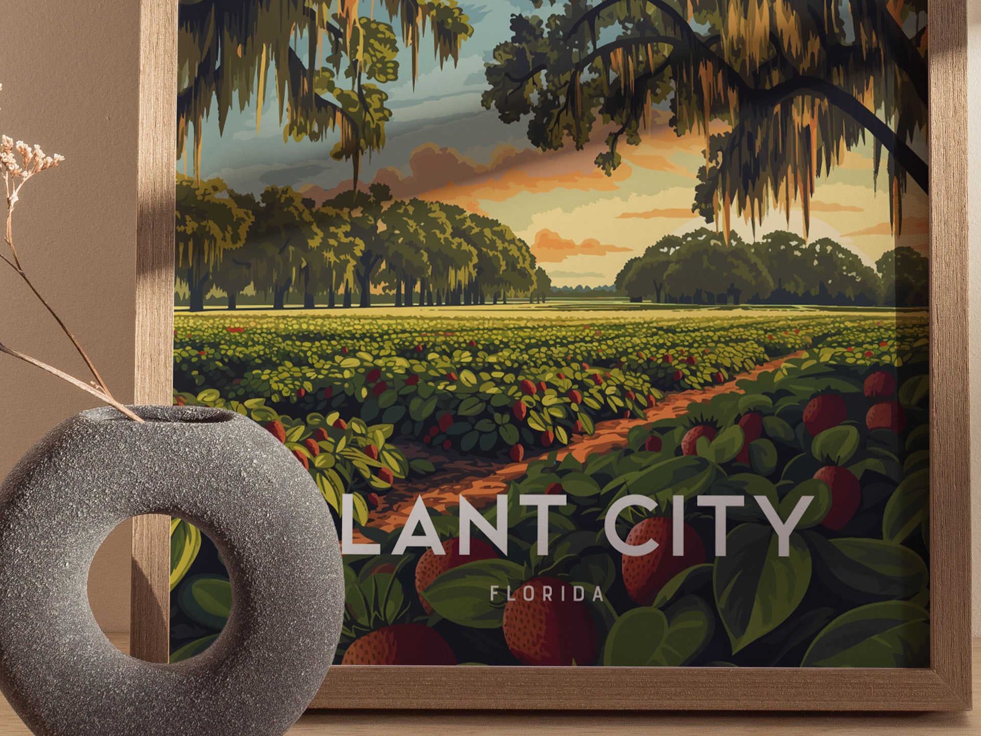 A framed poster displays strawberry fields under a sunrise sky with oak trees and Spanish moss, labeled Plant City Florida. A textured vase sits nearby.