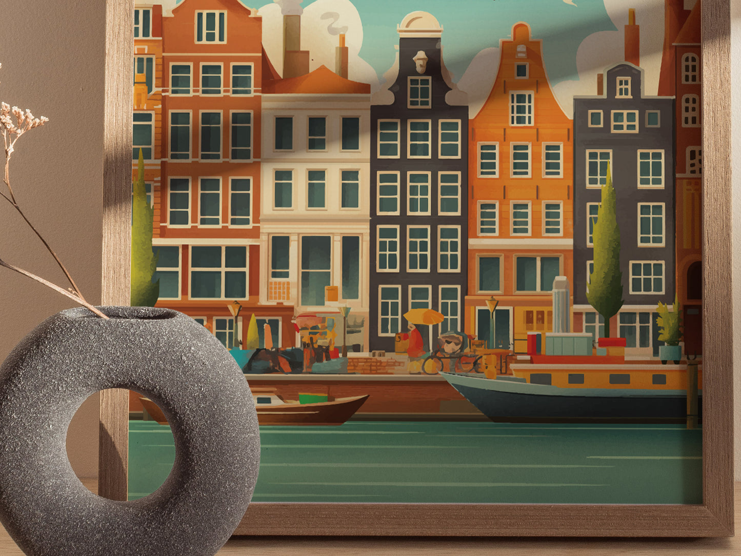 A framed artwork of Amsterdams colorful canal-side buildings is displayed beside a textured circular vase with dried grasses, creating a harmonious decorative setting.