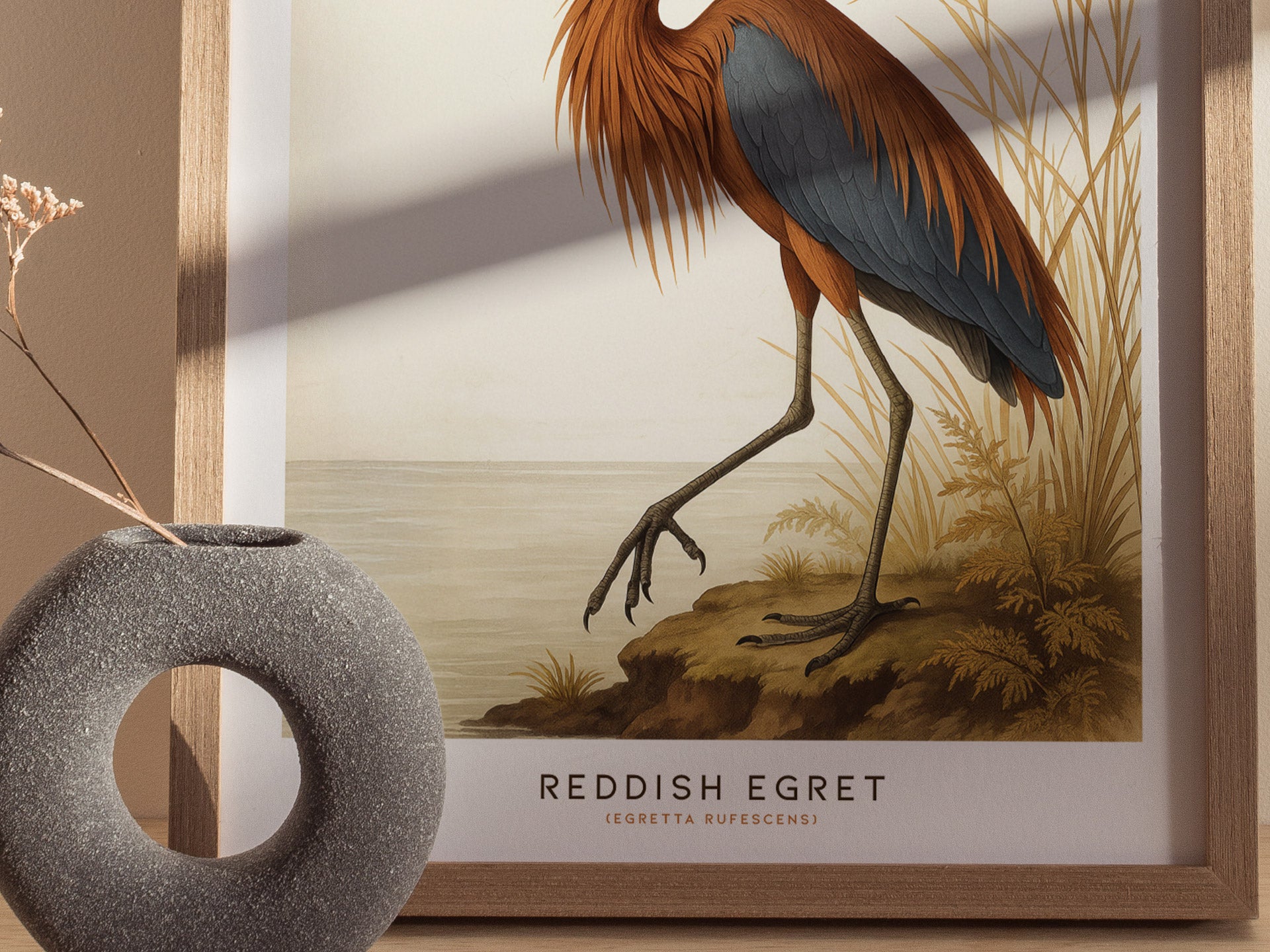 A close-up of a poster depicting a Reddish Egret with detailed plumage, framed in wood. The wall art is complemented by a textured, round vase holding dried flowers, creating a natural, artistic display.