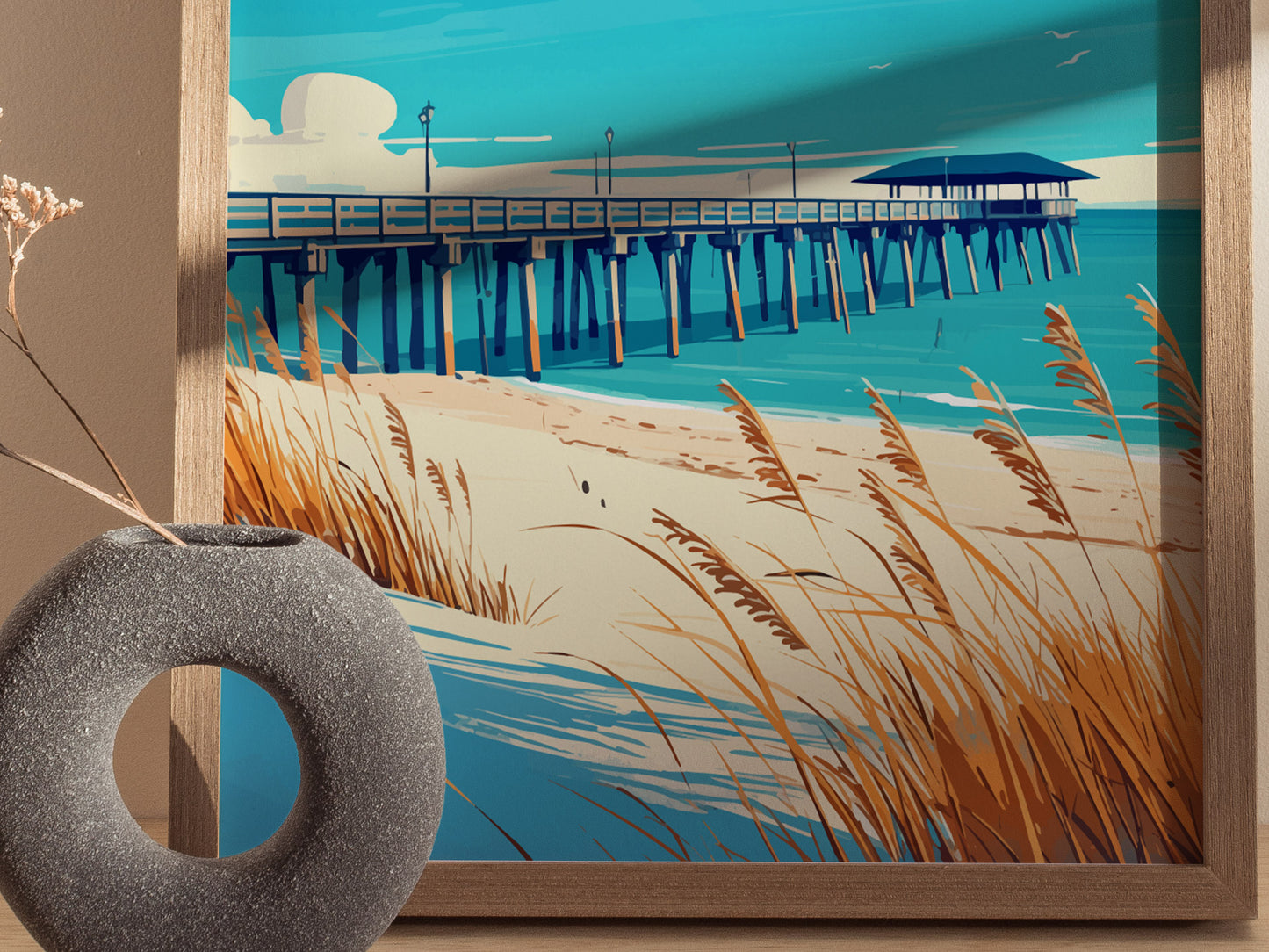 A framed poster depicts a scenic beach with a long pier extending over turquoise waters, surrounded by sandy dunes and swaying sea oats. A round, textured gray vase is visible.