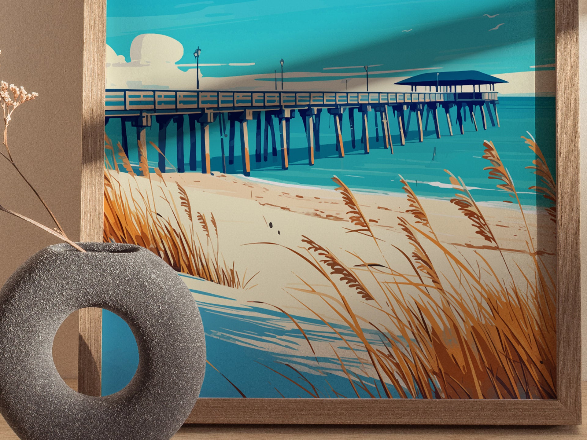 A framed poster depicts a scenic beach with a long pier extending over turquoise waters, surrounded by sandy dunes and swaying sea oats. A round, textured gray vase is visible.