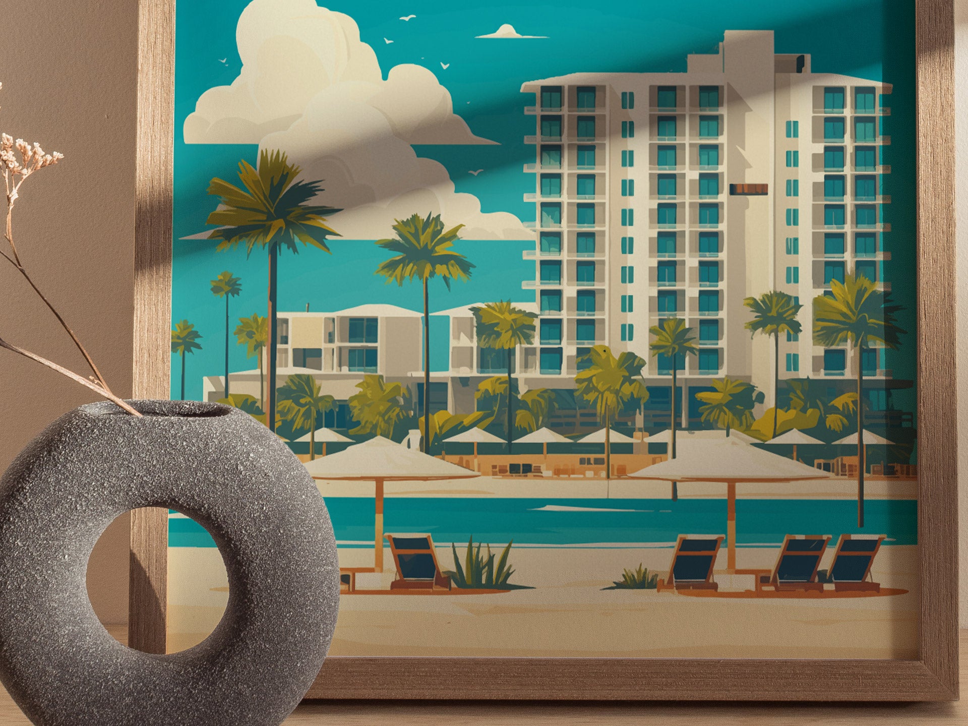 A framed poster depicts a coastal scene with a tall building, palm trees, and beach chairs under umbrellas. A round, textured vase with dried flowers is in the foreground.