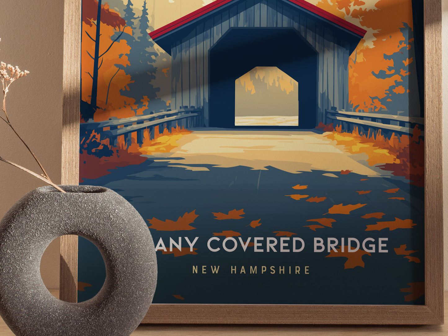 A framed poster of the Albany Covered Bridge in New Hampshire showcases the iconic structure set against a backdrop of vibrant autumn foliage. The warm colors of the leaves and the tranquil river create a picturesque fall scene.