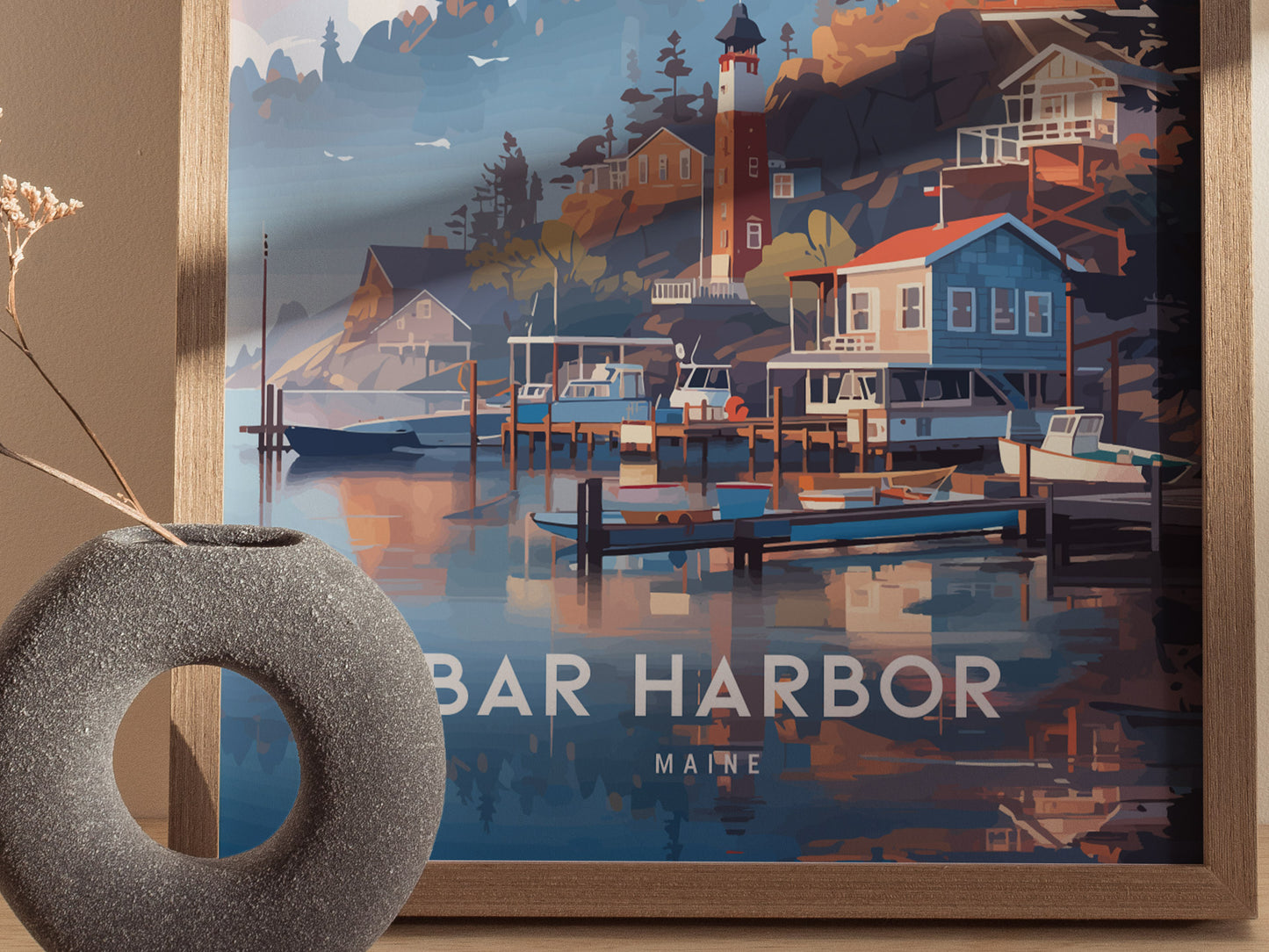 A framed poster of Bar Harbor, Maine features a scenic coastal view with boats, a lighthouse, and charming buildings. A round, textured vase with dried branches is in the foreground.