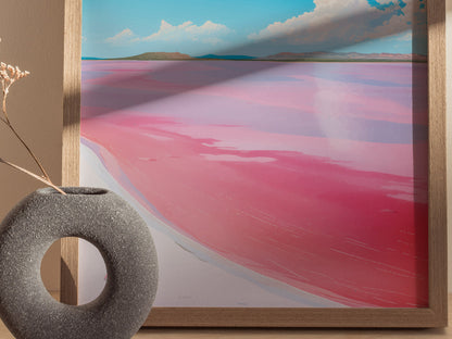 A framed poster depicts Lake Hillier with vibrant pink water contrasting against a blue sky, accompanied by a textured gray vase holding dry flowers in the foreground.