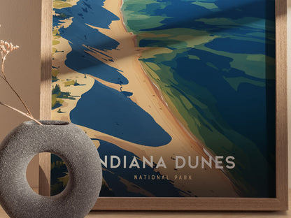 A framed poster of Indiana Dunes National Park with abstract shapes depicting dunes and water, complemented by a textured gray vase with dried flowers in the foreground.