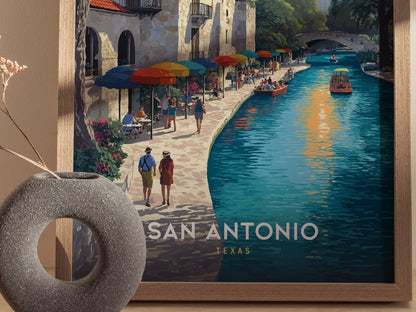 A framed artwork depicts a vibrant San Antonio riverwalk scene with colorful umbrellas, people strolling, and boats on the water. A textured vase with dried flowers is in the foreground.