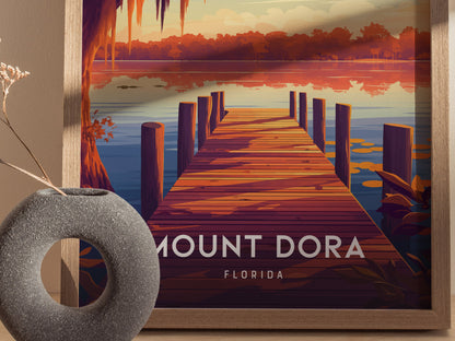 A framed poster features a vibrant illustration of a wooden dock extending into a serene lake at sunset, with Mount Dora, Florida text.