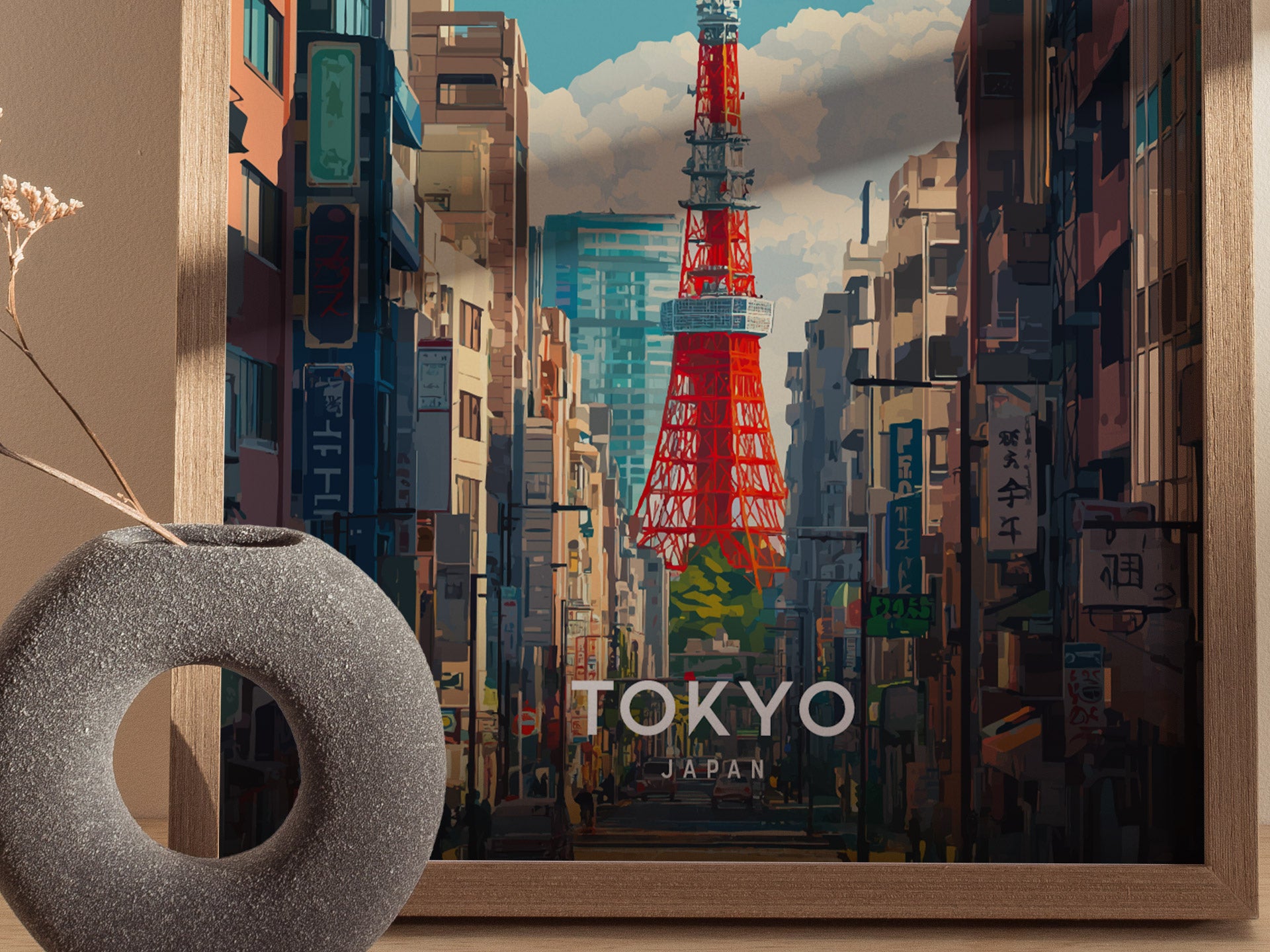 A framed poster depicts Tokyo Tower rising above a bustling city street, surrounded by tall buildings under a cloudy sky. A round, textured vase with dried flowers sits nearby.