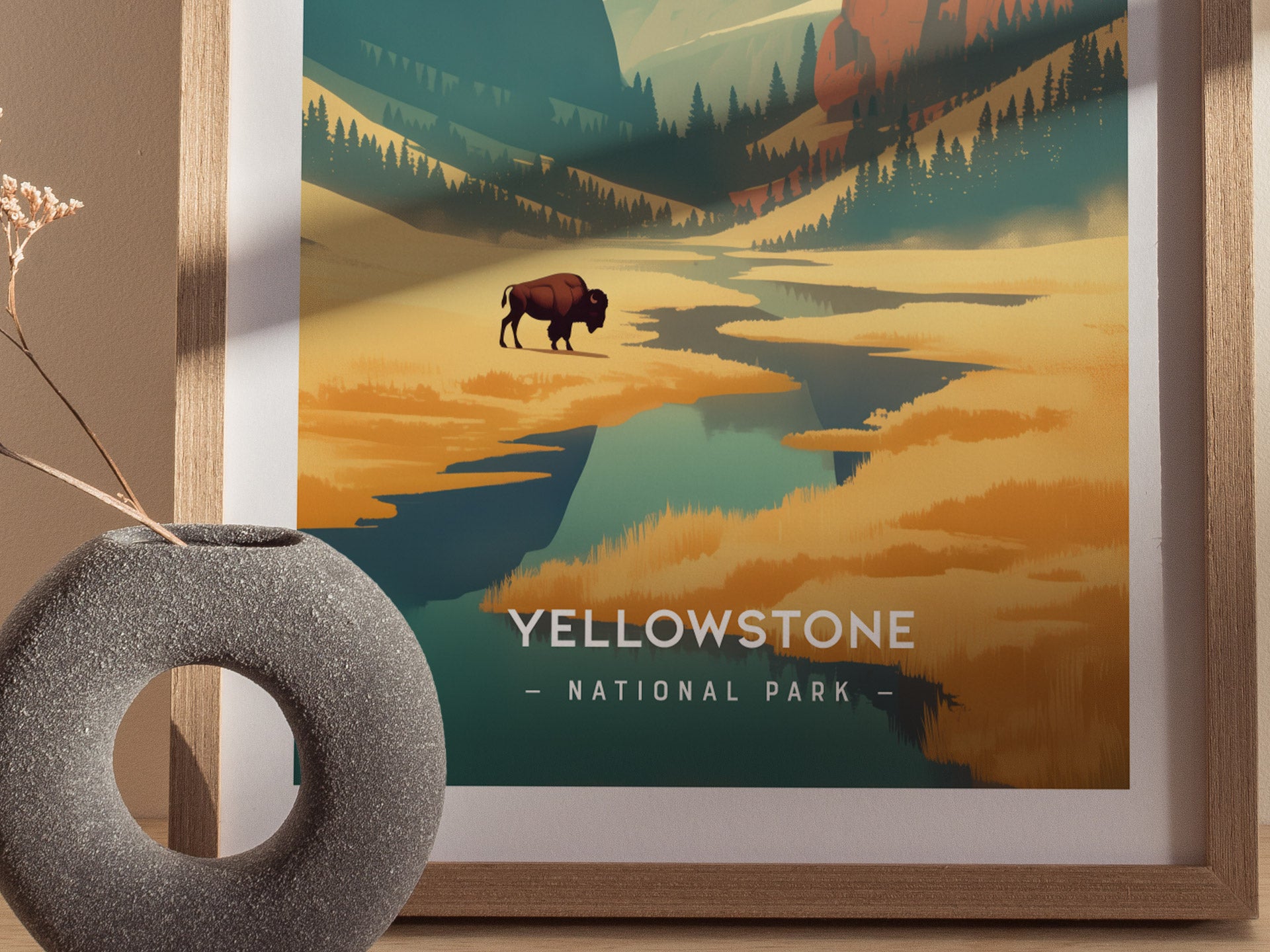 A framed poster of Yellowstone National Park features a minimalist design with a buffalo, forested valleys, and mountains. A round stone vase with dried flowers sits nearby.