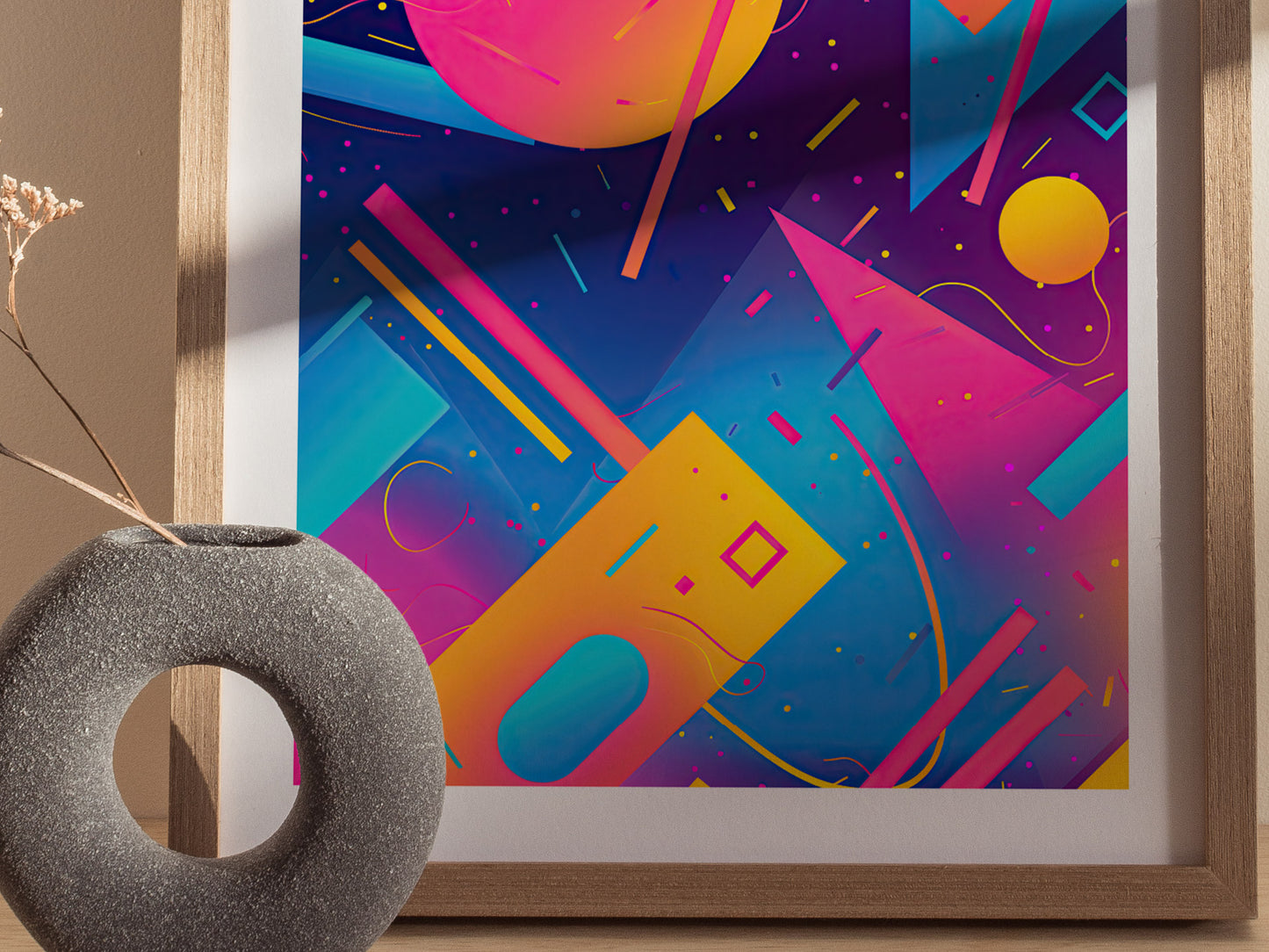 A colorful 90s aesthetic poster featuring bold geometric shapes in vibrant pinks, yellows, and blues is displayed in a wooden frame. A round, textured vase sits nearby.